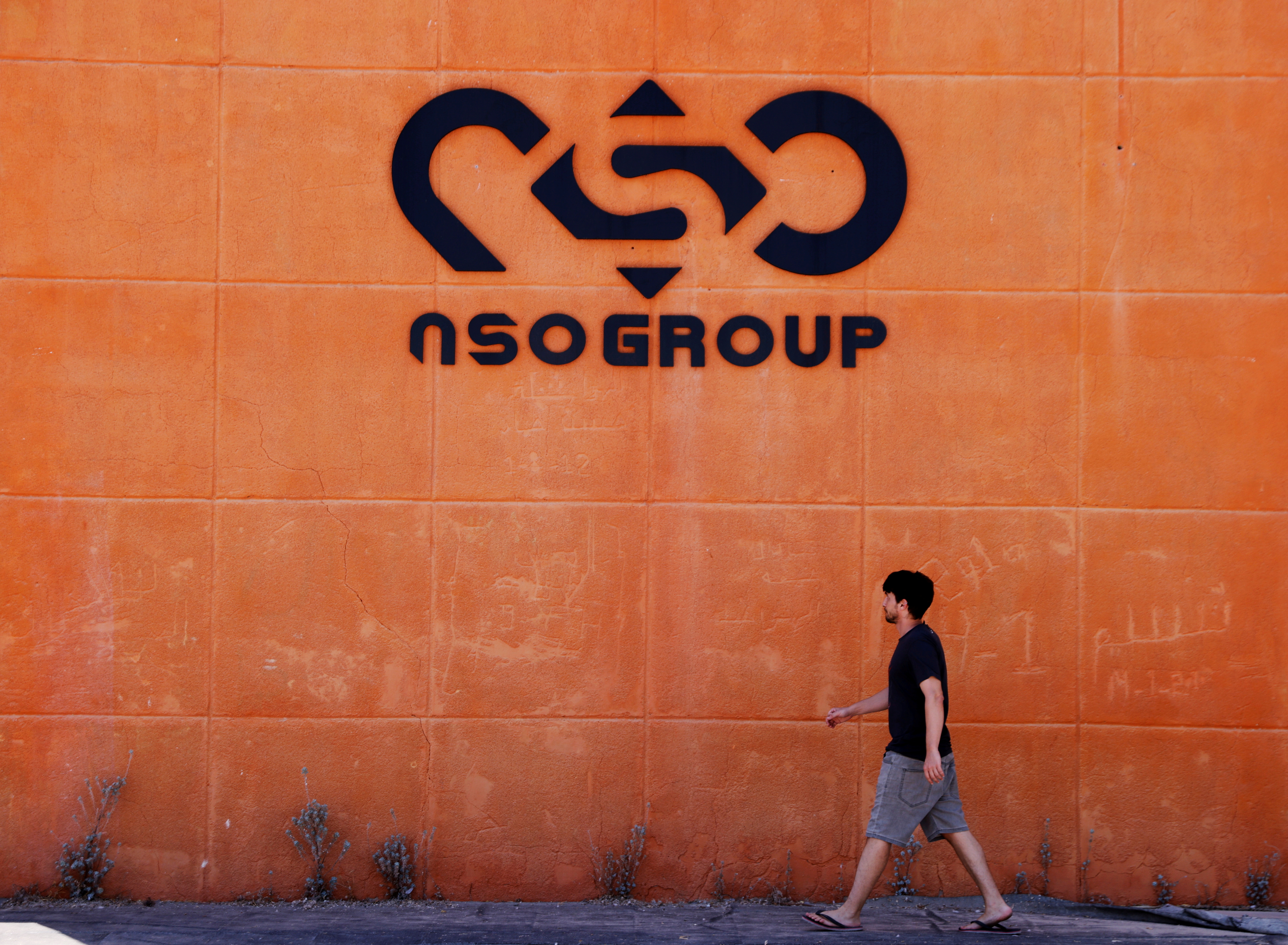 A man walks past the logo of Israeli cyber-firm NSO Group at one of its branches in the Arava Desert in Israel on July 22, 2021 [File: Reuters/Amir Cohen]