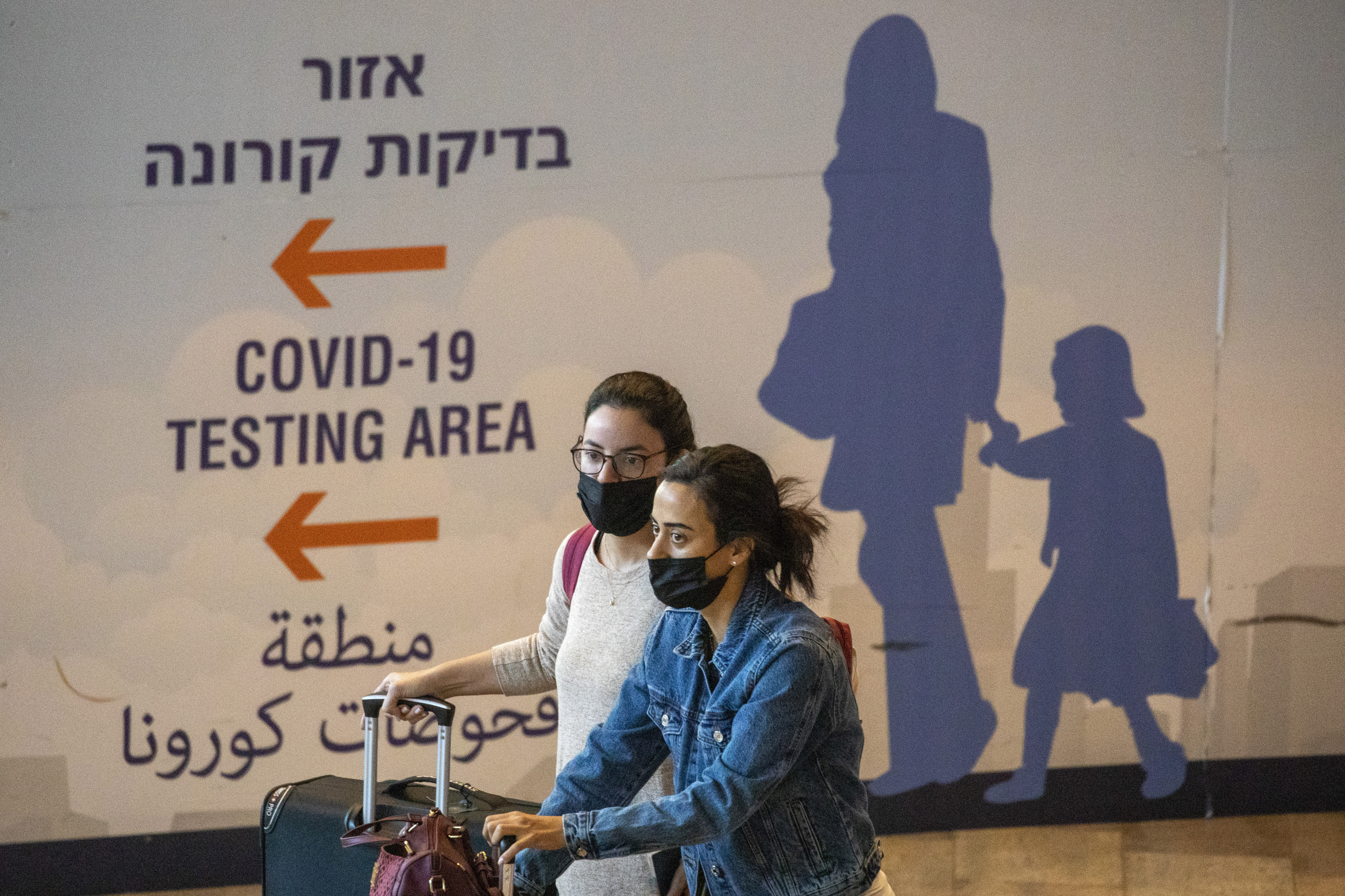 Travelers wearing protective face masks arrive at Ben Gurion Airport near Tel Aviv, Israel, Sunday, Nov. 28, 2021. Israel on Sunday approved barring entry to foreign nationals and the use of controversial technology for contact tracing as part of its efforts to clamp down on a new coronavirus variant