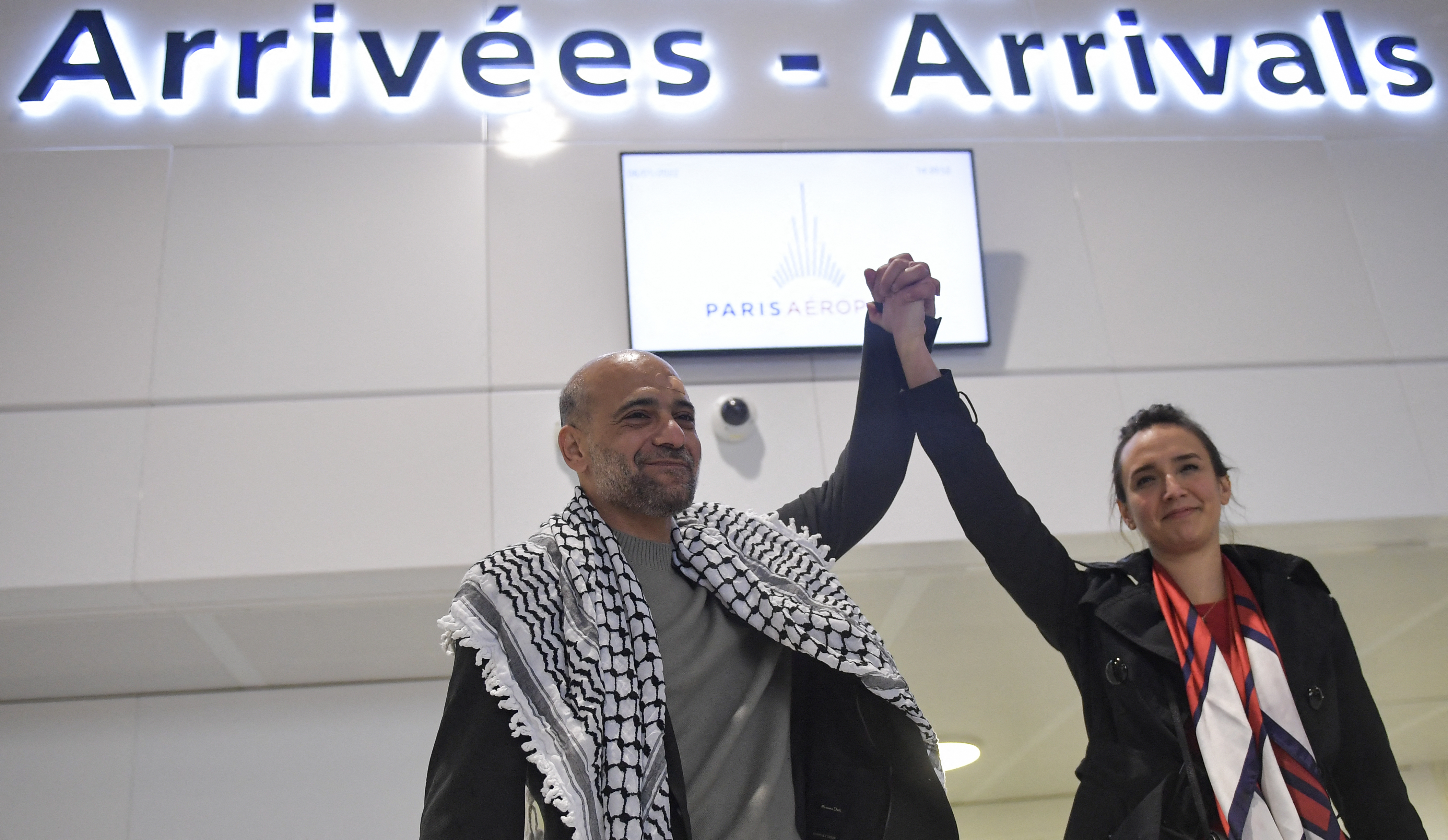 Egyptian-Palestinian activist Ramy Shaath holds up the arm of his wife Celine Lebrun-Shaath as he arrives at Roissy airport in Roissy, outside Paris, on January 8, 2022.