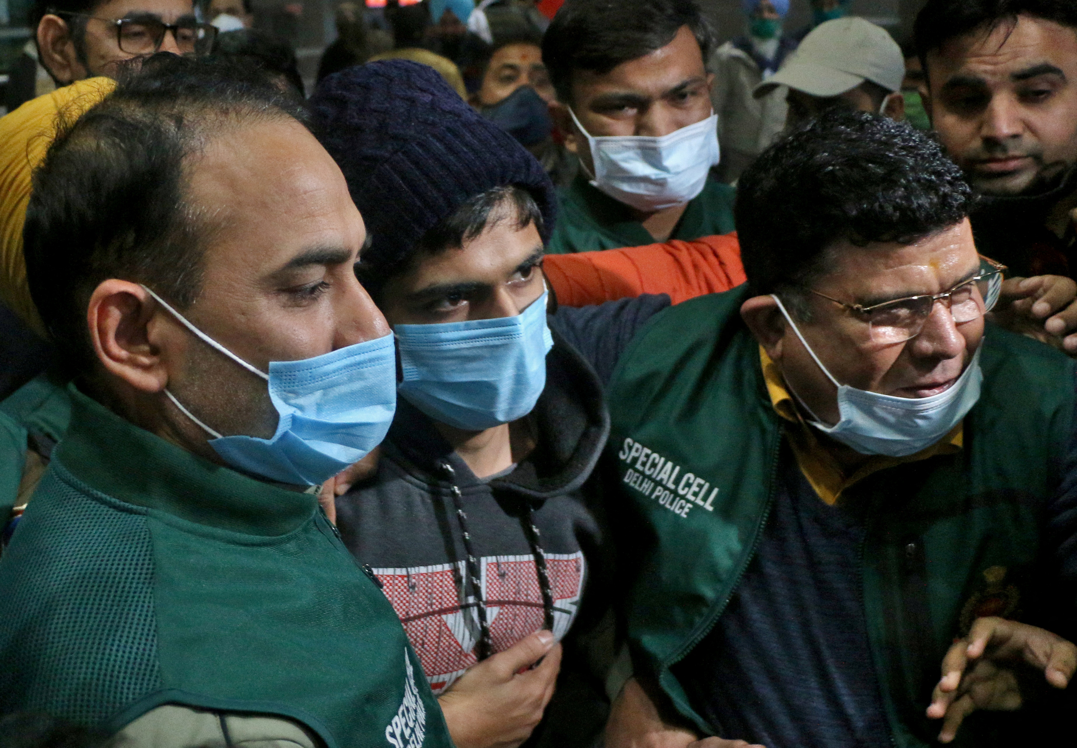 Police escort a 20-year-old man in New Delhi airport for alleged involvement in online abuse in Assam