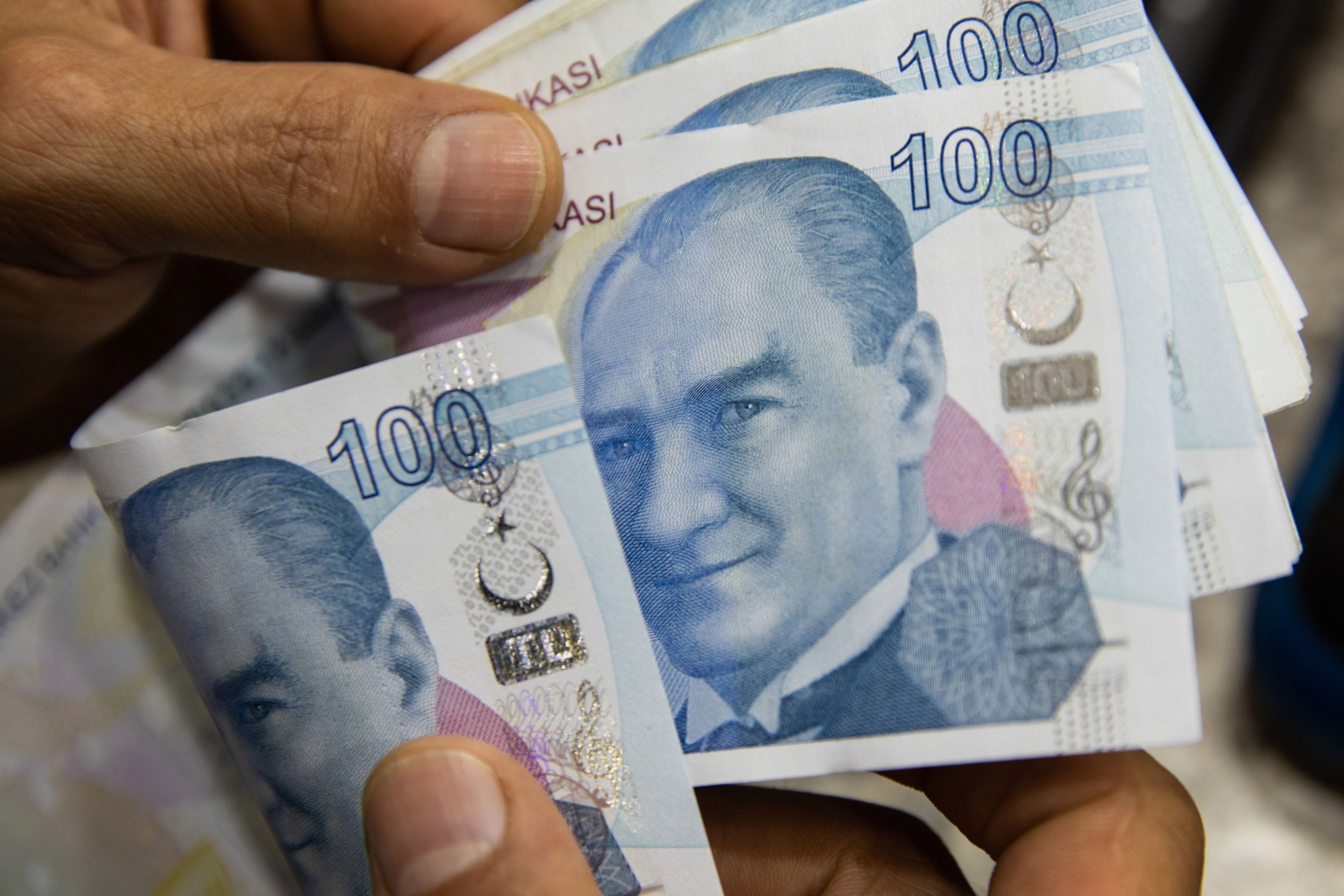 An employee hands 100 Turkish lira banknotes to a customer on the counter inside a foreign currency exchange bureau in the Beyoglu district of of Istanbul, Turke
