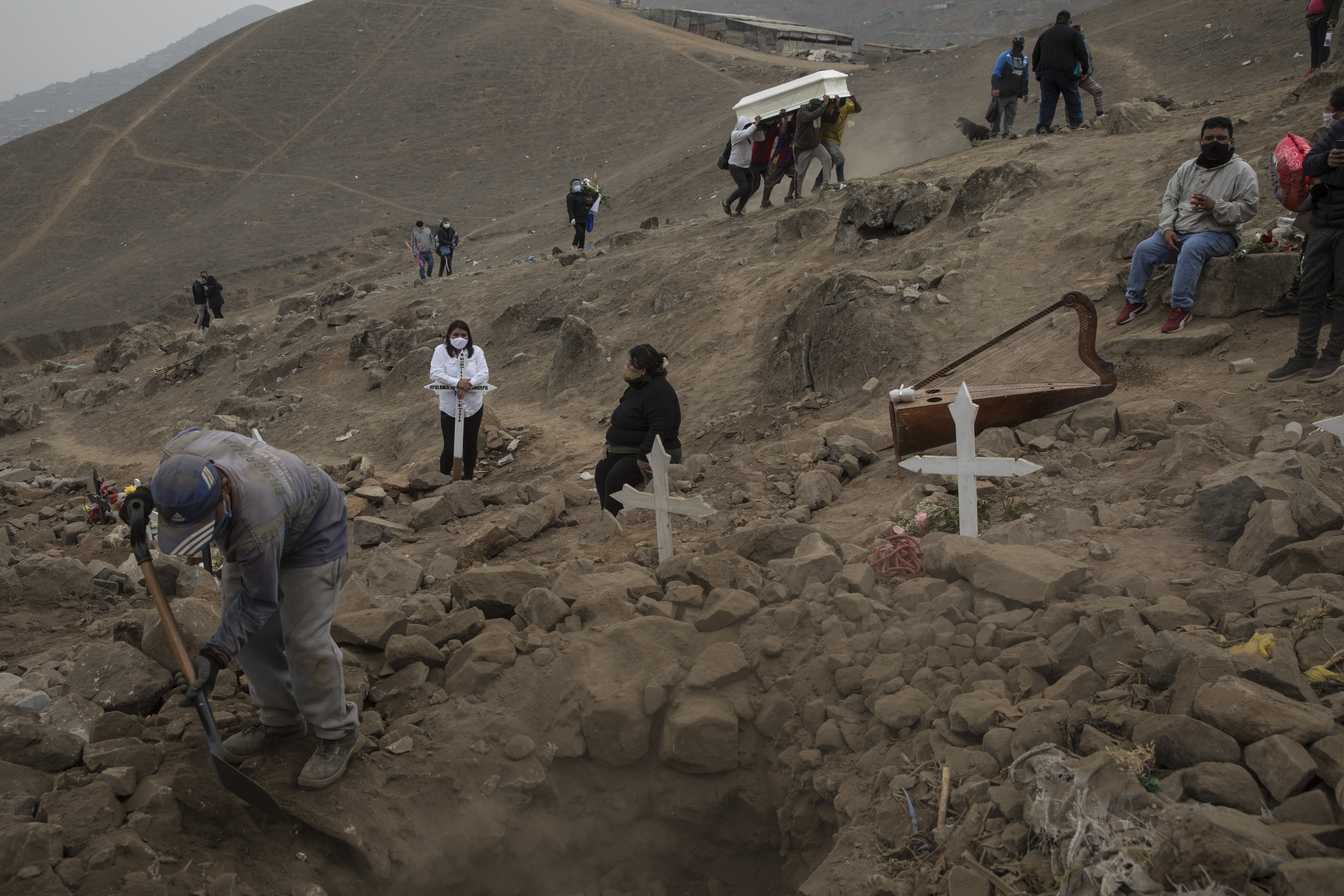 A cemetery worker shovels dirt into a grave that contains the remains of Apolonia Uanampa who died from the new coronavirus, as the coffin that contains the remains of Demetria Huamani, also a victim of the virus, is carried to her burial site at the Nueva Esperanza cemetery on the outskirts of Lima, Peru,