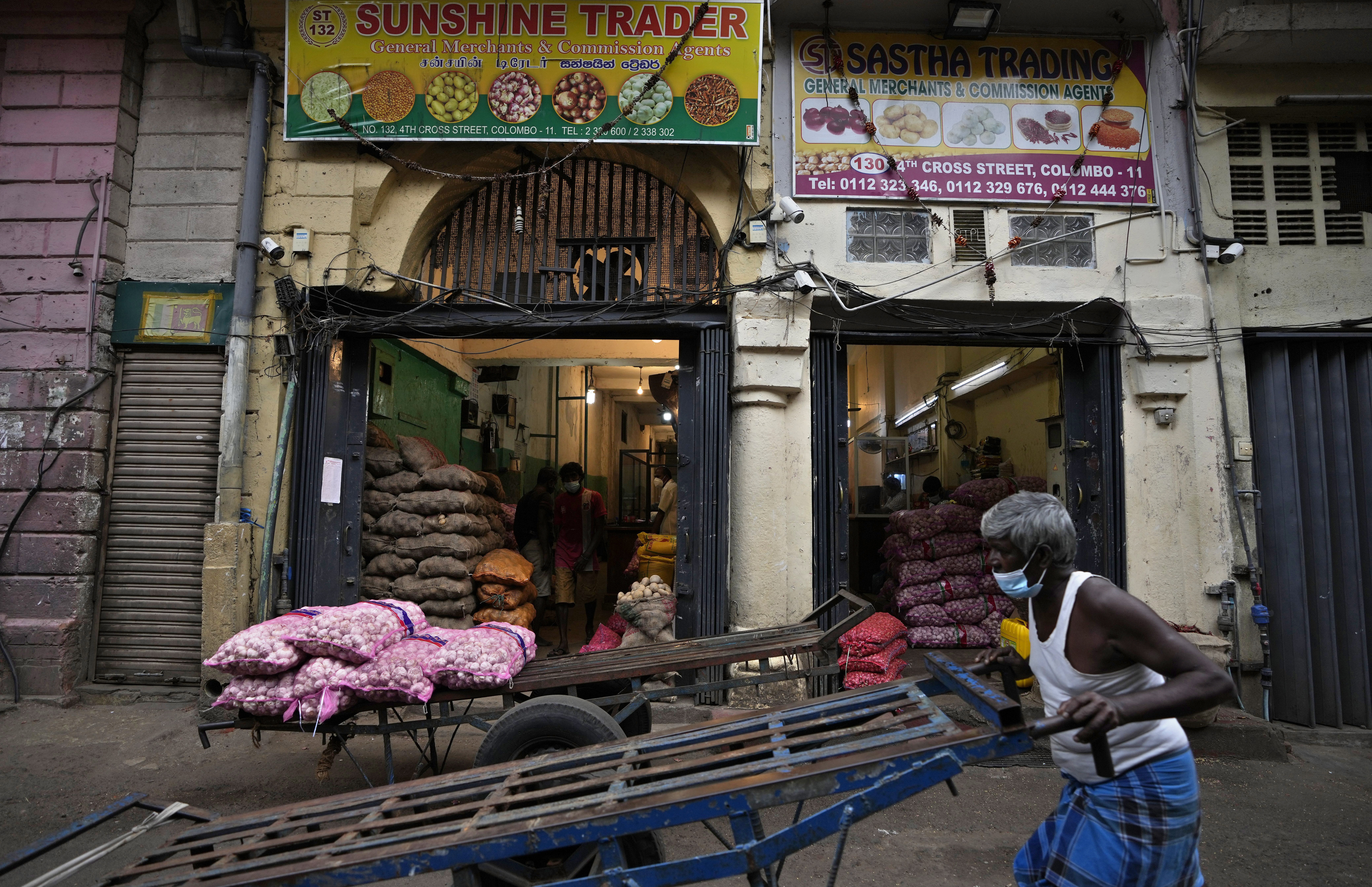 A Sri Lankan laborer pushes his cart past shops selling vegetables at a wholesale market