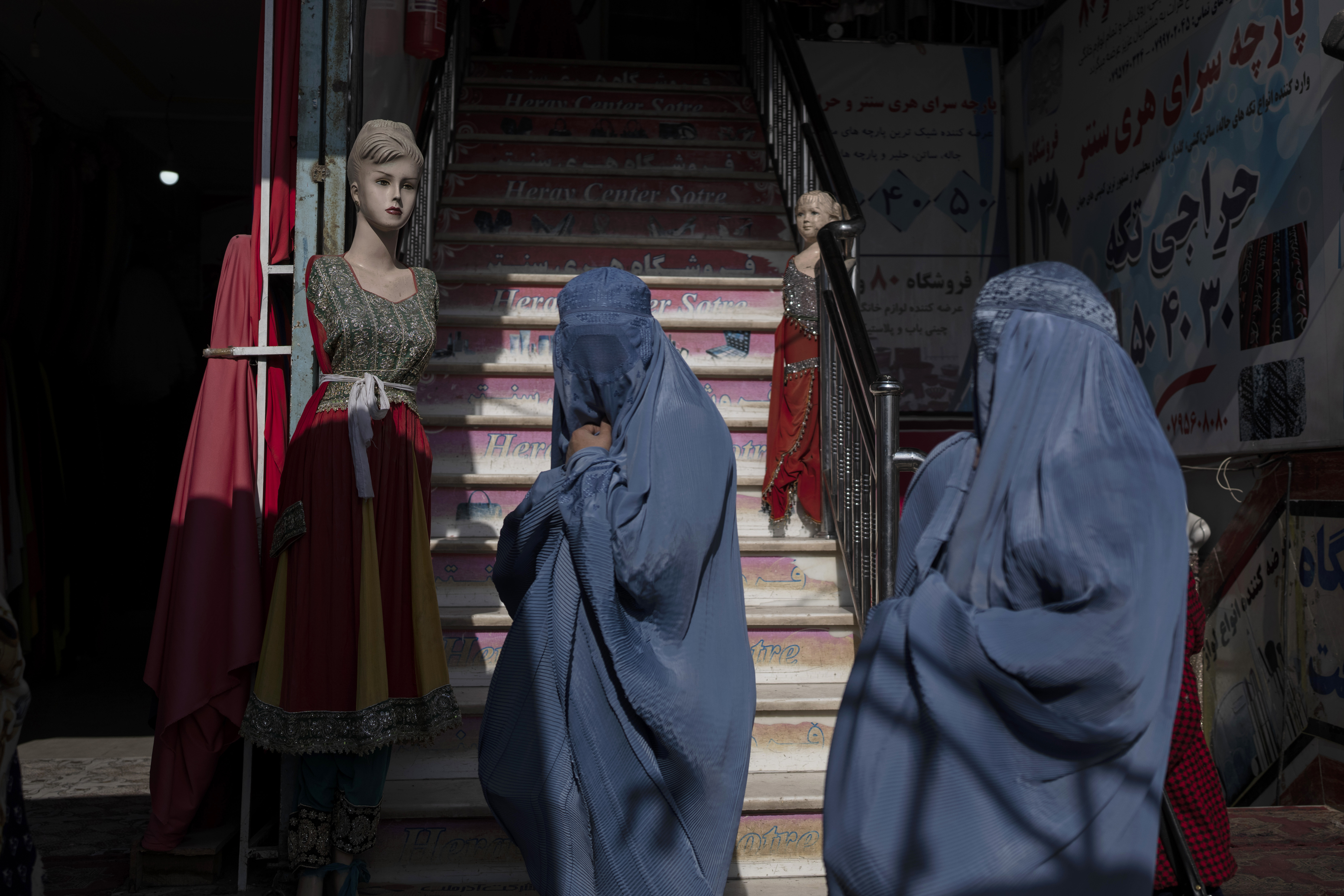 Burka-wearing Afghan women walk past a clothing shop, in Herat
