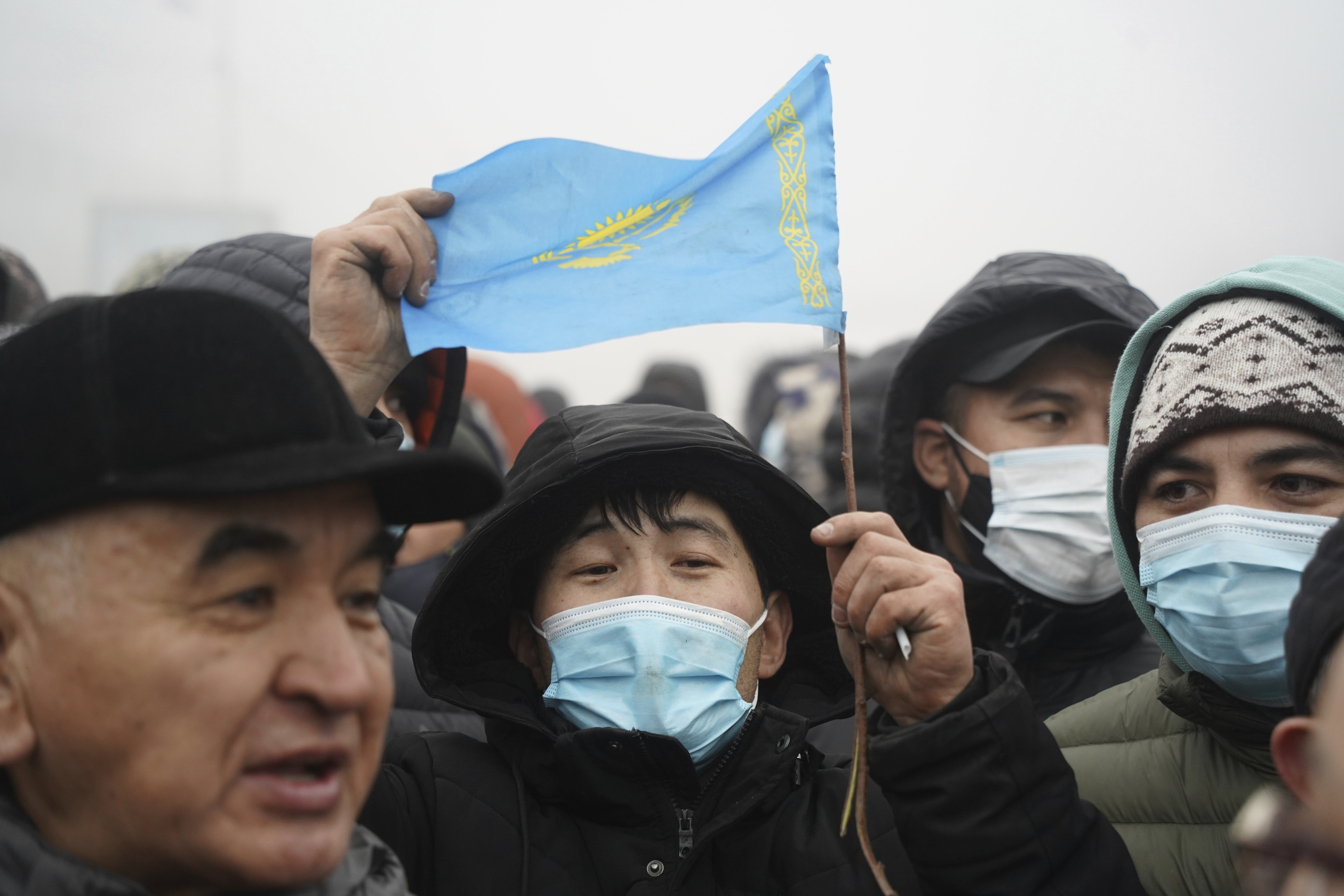 A Kazakh man holds up a flag of Kazakhstan amid a crowd of protesters