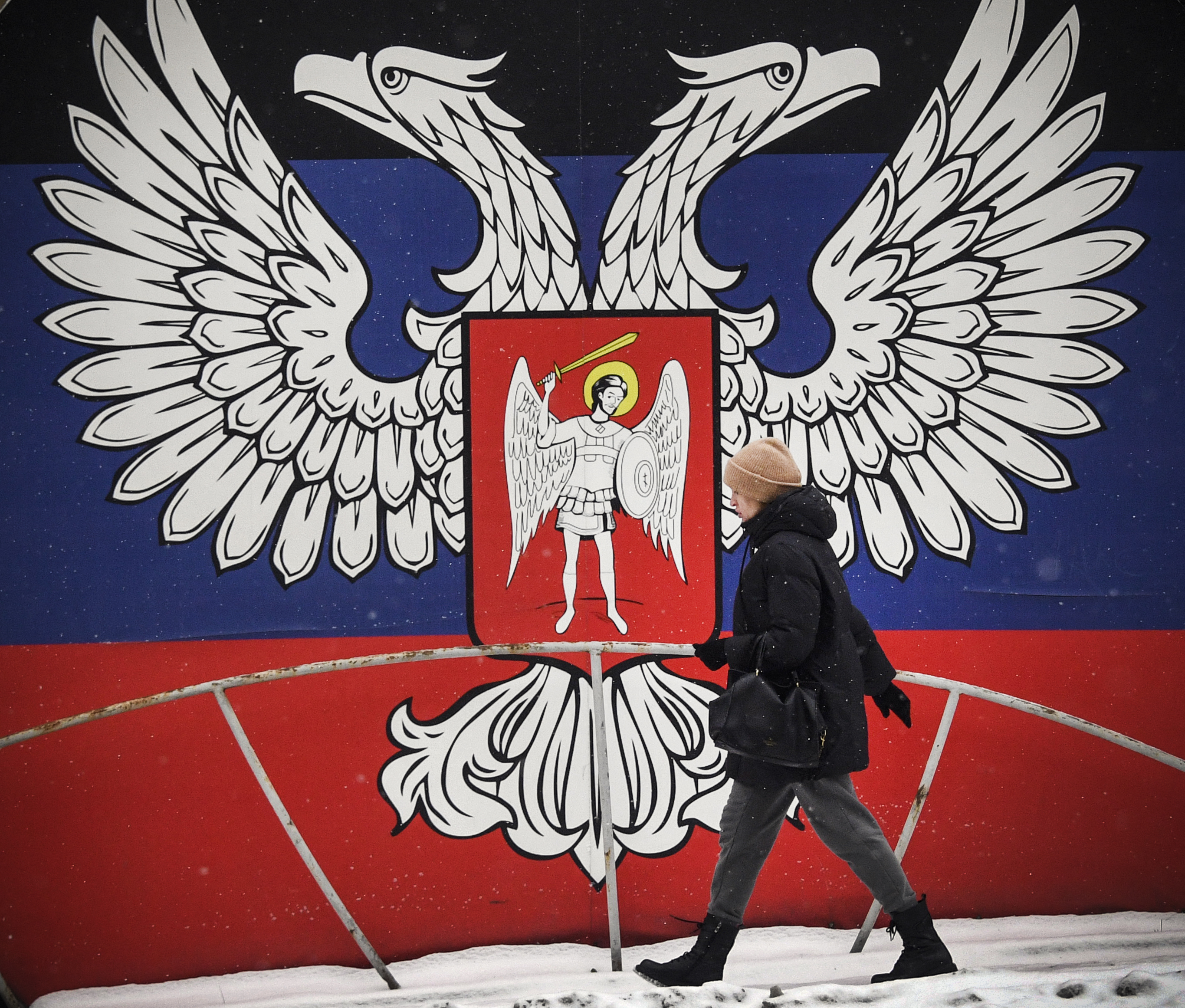 In this file photo taken on January 19, 2022, a pedestrian walks past a huge state emblem of the self-proclaimed Donetsk People's Republic in Donetsk, eastern Ukraine