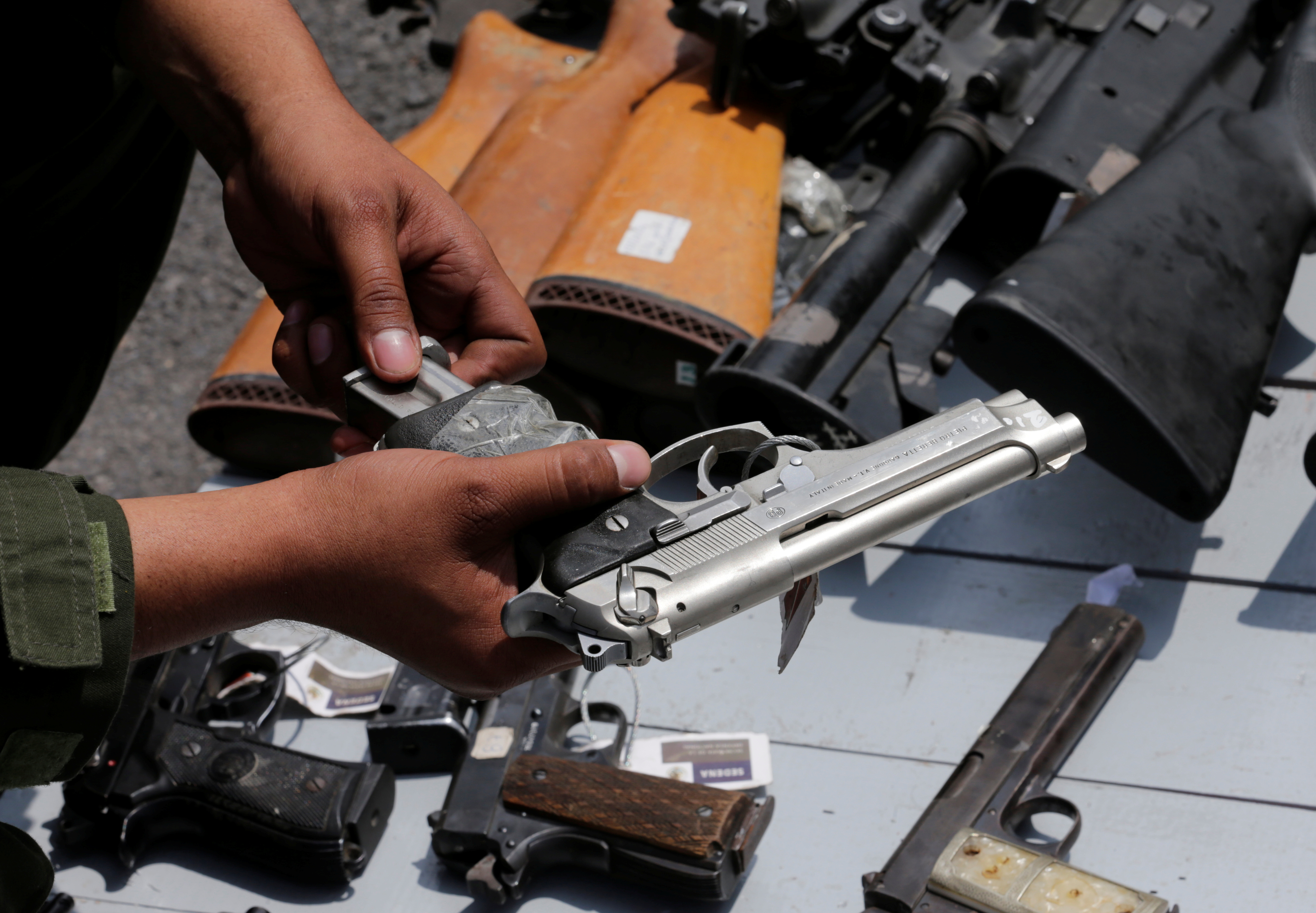 A Mexican soldier holds up a gun next to other weapons seized from alleged drug traffickers or handed in by residents before they are destroyed at a military zone in Mexico City,