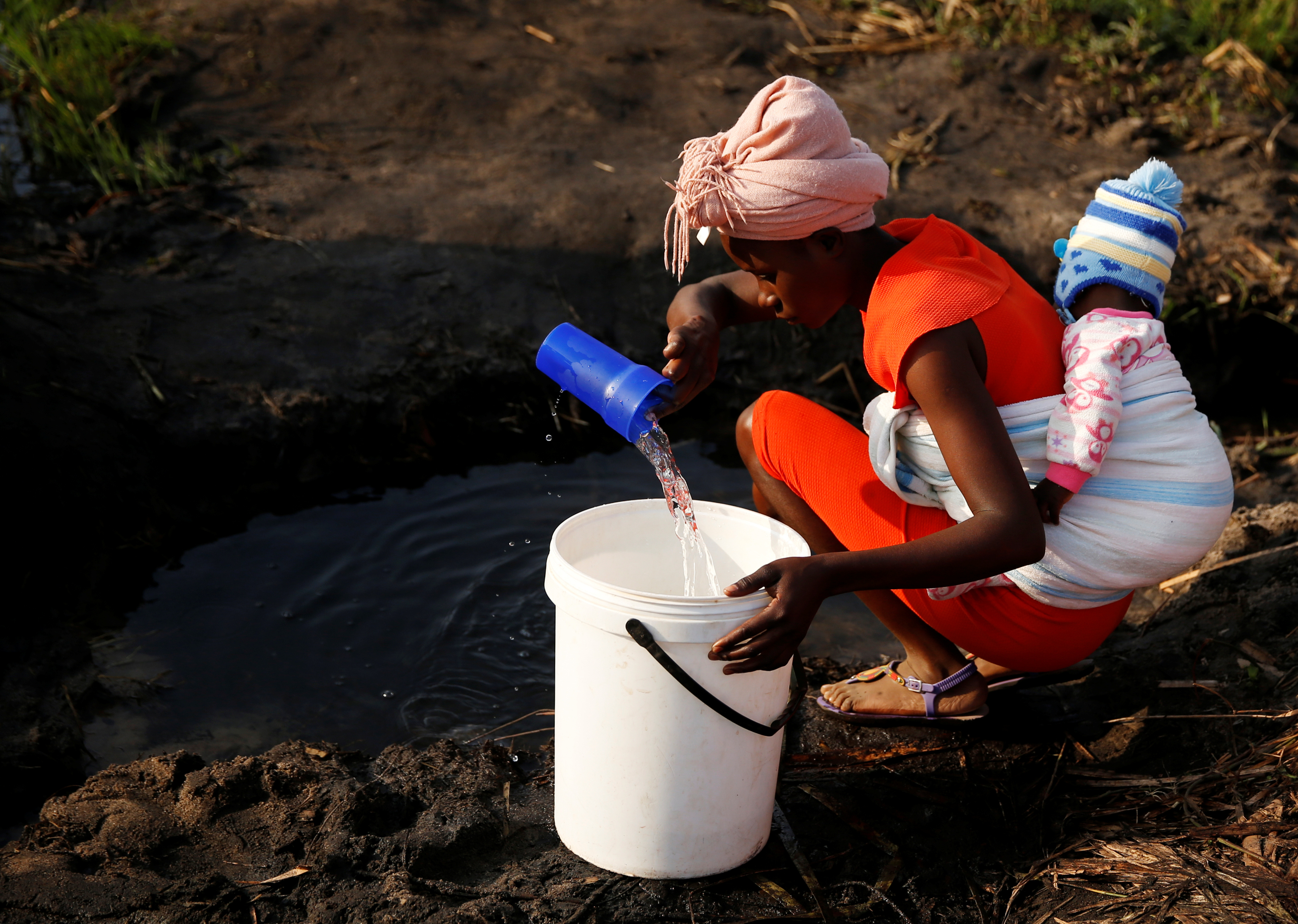A woman with a baby on her back collects water in Mabvuku, a highly-populated suburb in Harare, Zimbabwe
