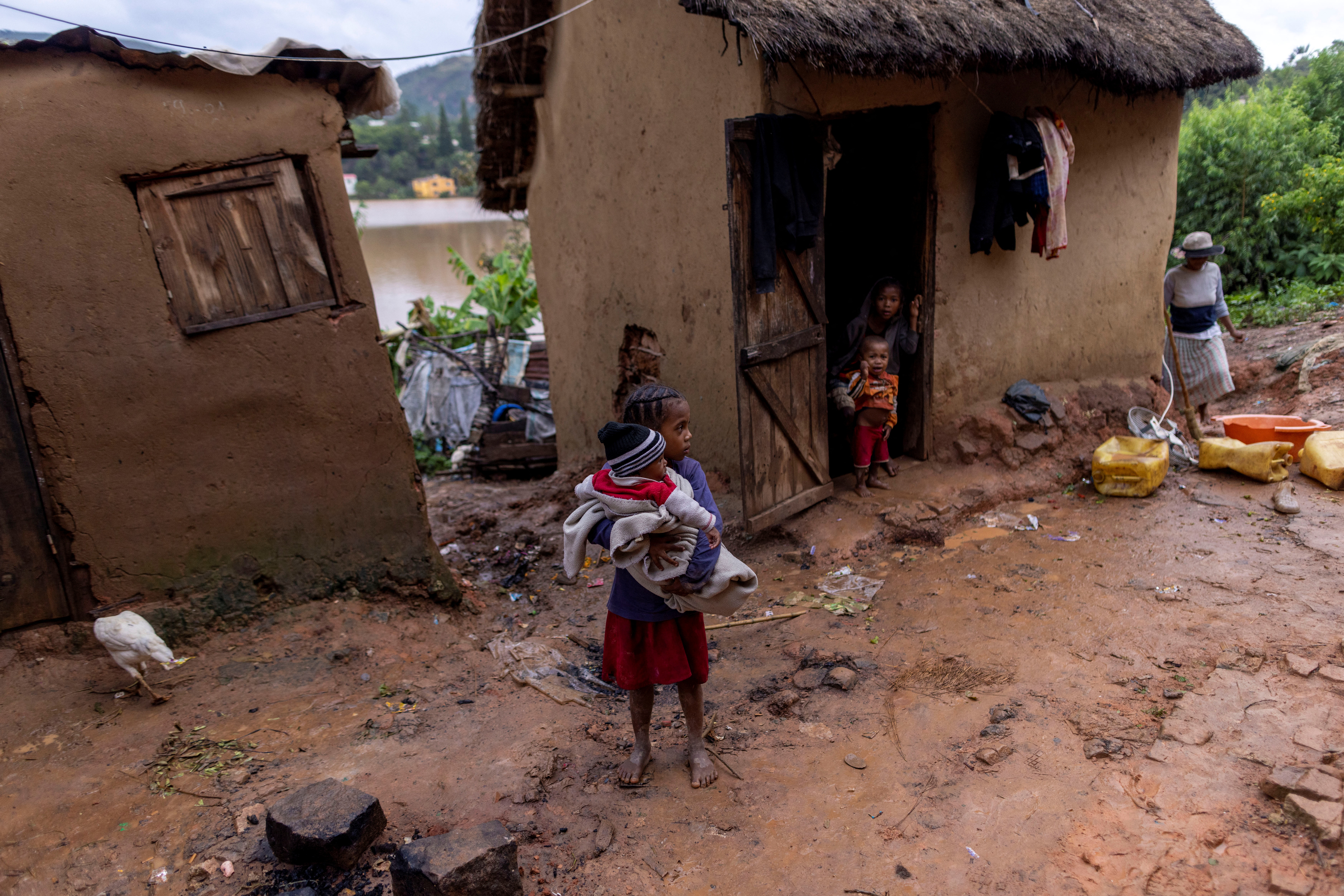 A girl holds a baby outside a damaged house in a flooded area