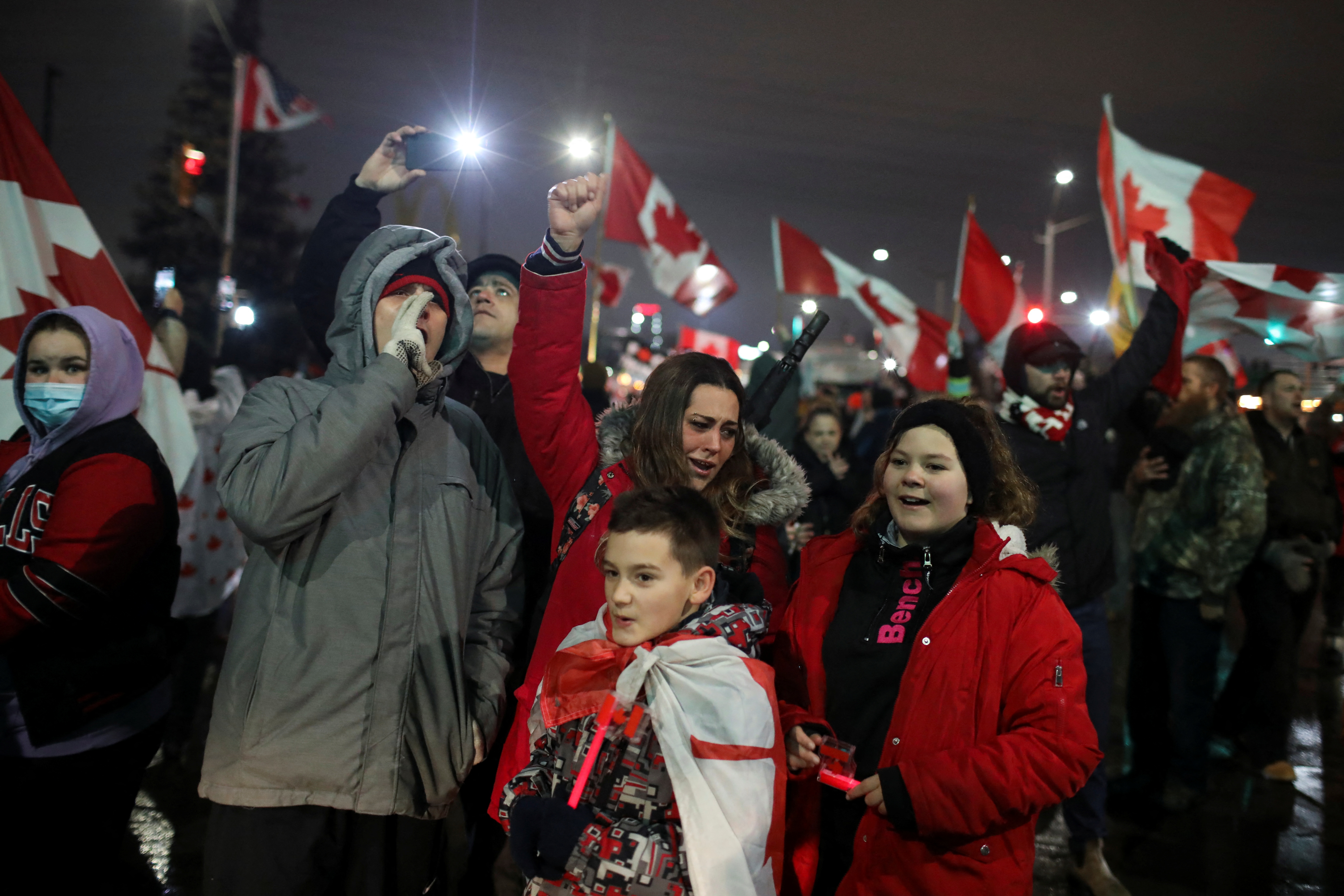 People cheer and wave Canadian flags in support of truckers blocking access to the Ambassador Bridge