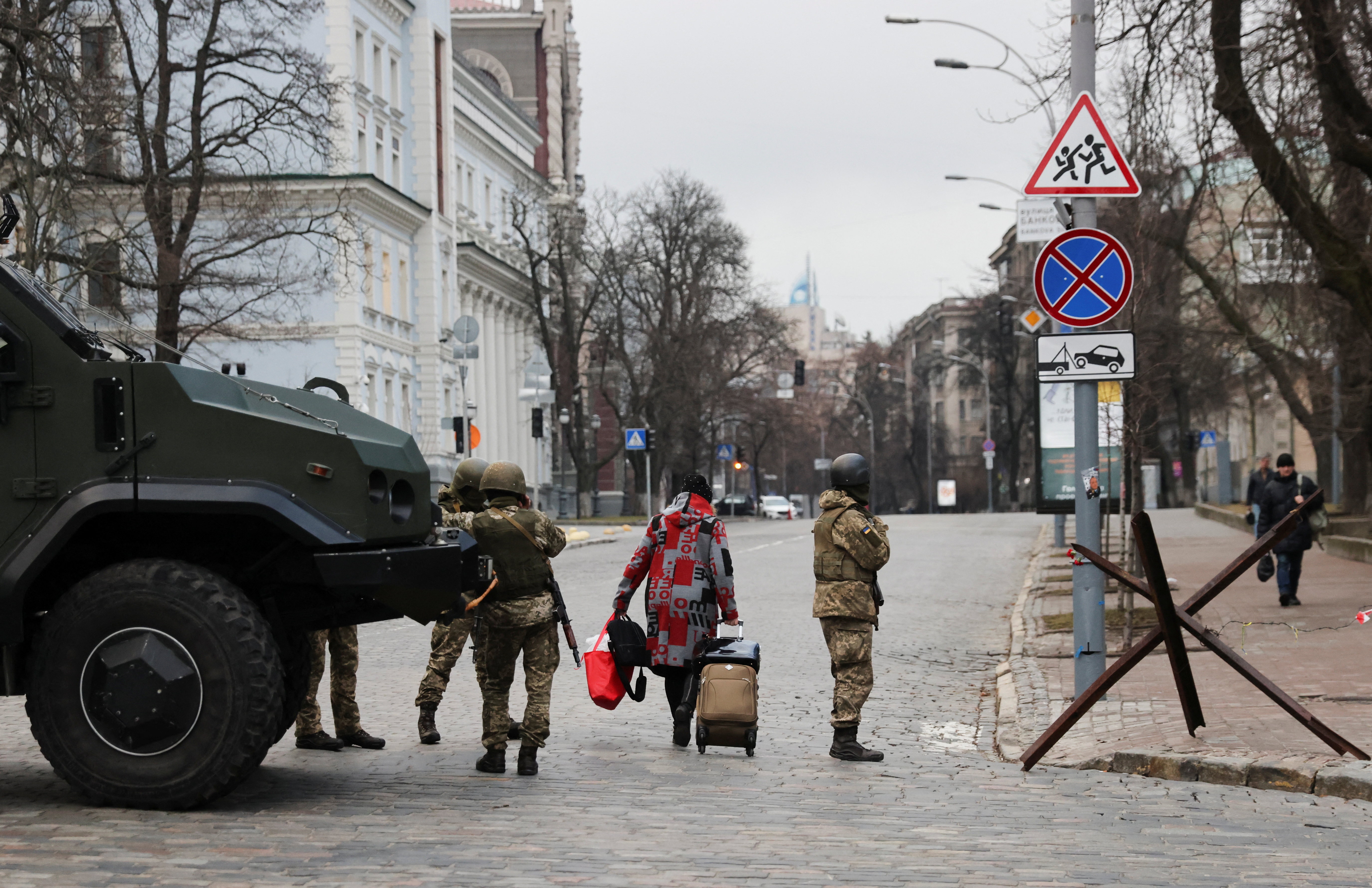 A woman walks past Ukrainian military service members guarding a road that leads to a government block