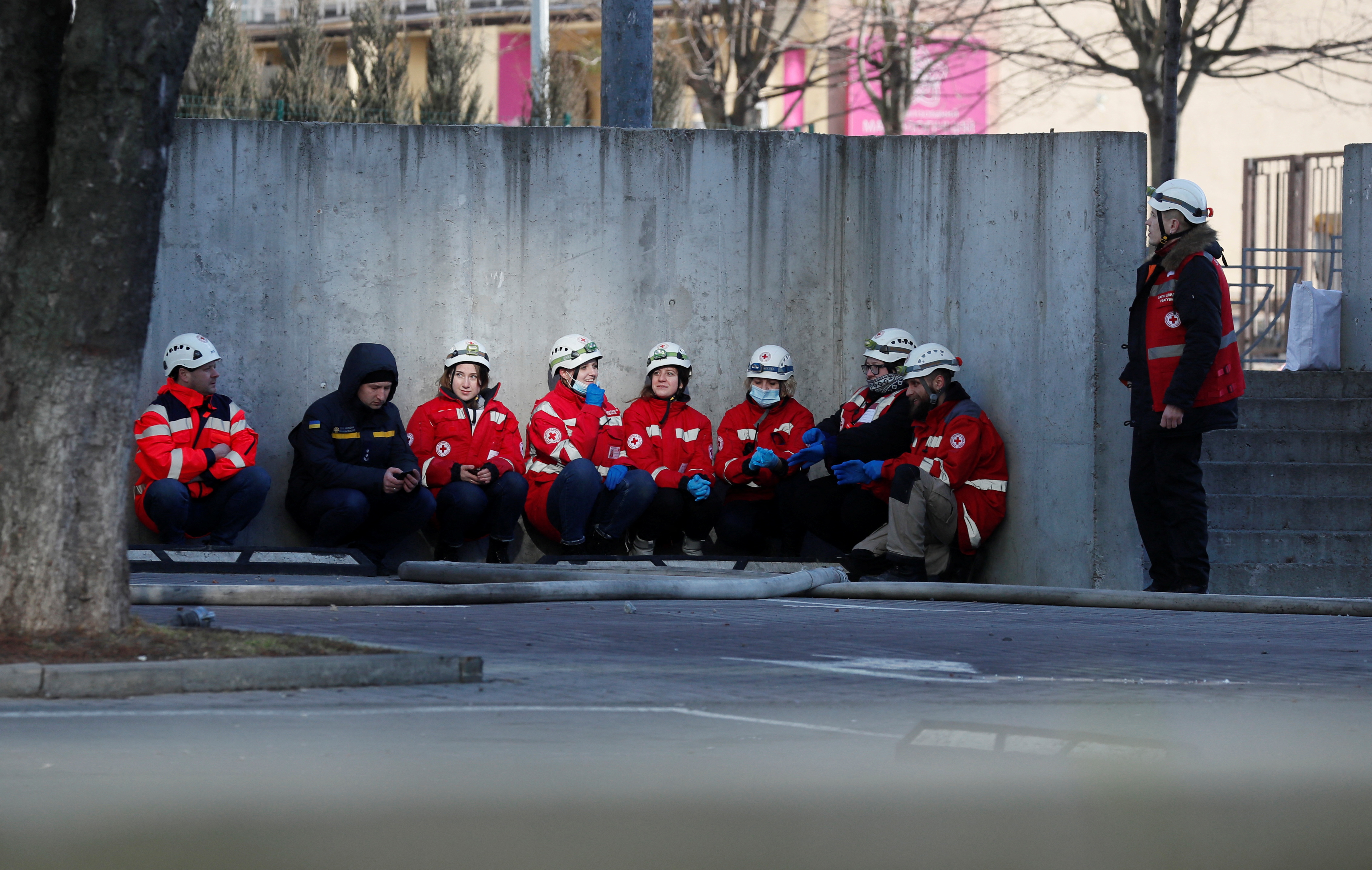 Paramedics take cover as an air-raid siren sounds, near an apartment building damaged by recent shelling in Kyiv