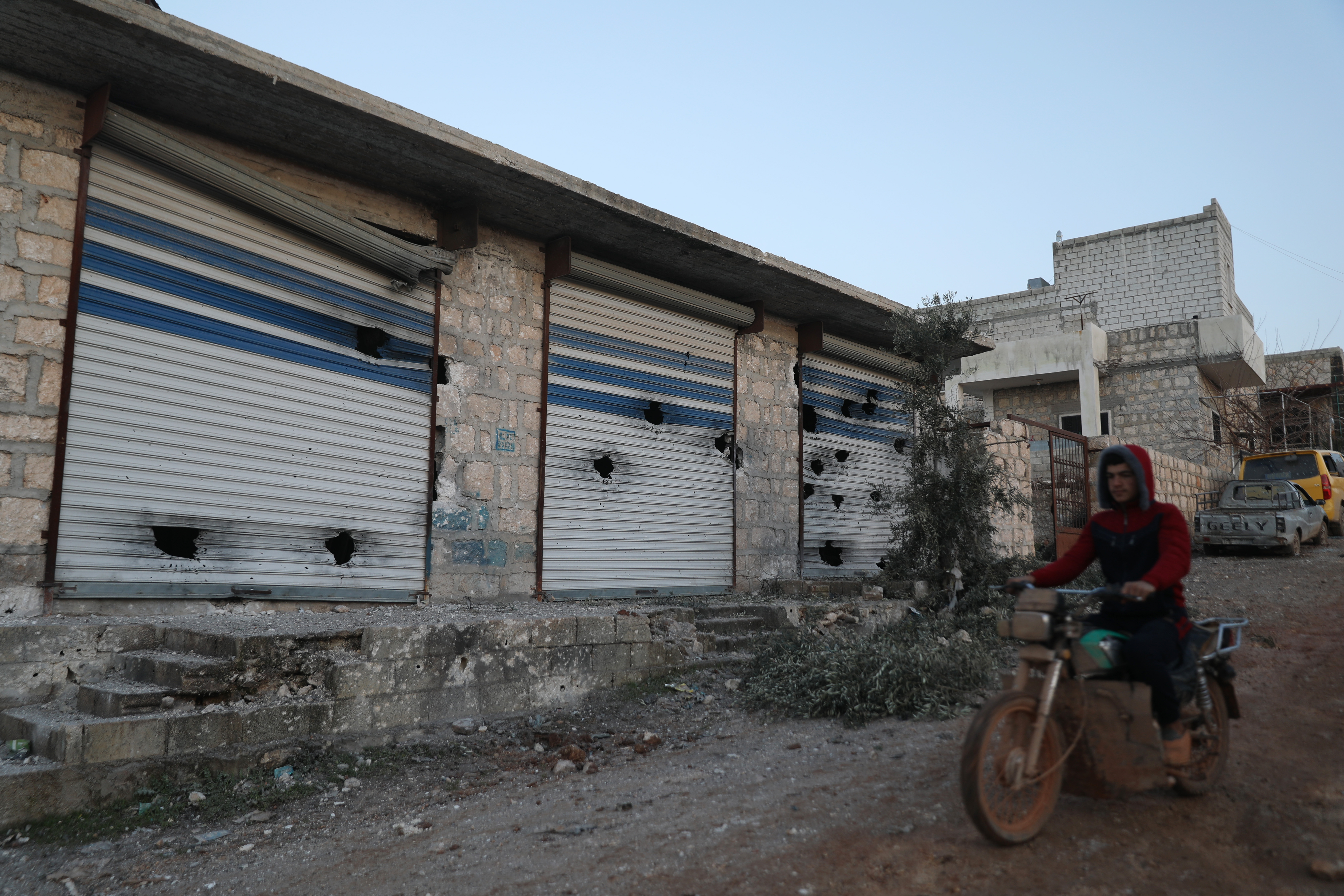 A Syrian man rides his motorcycle along damaged shops
