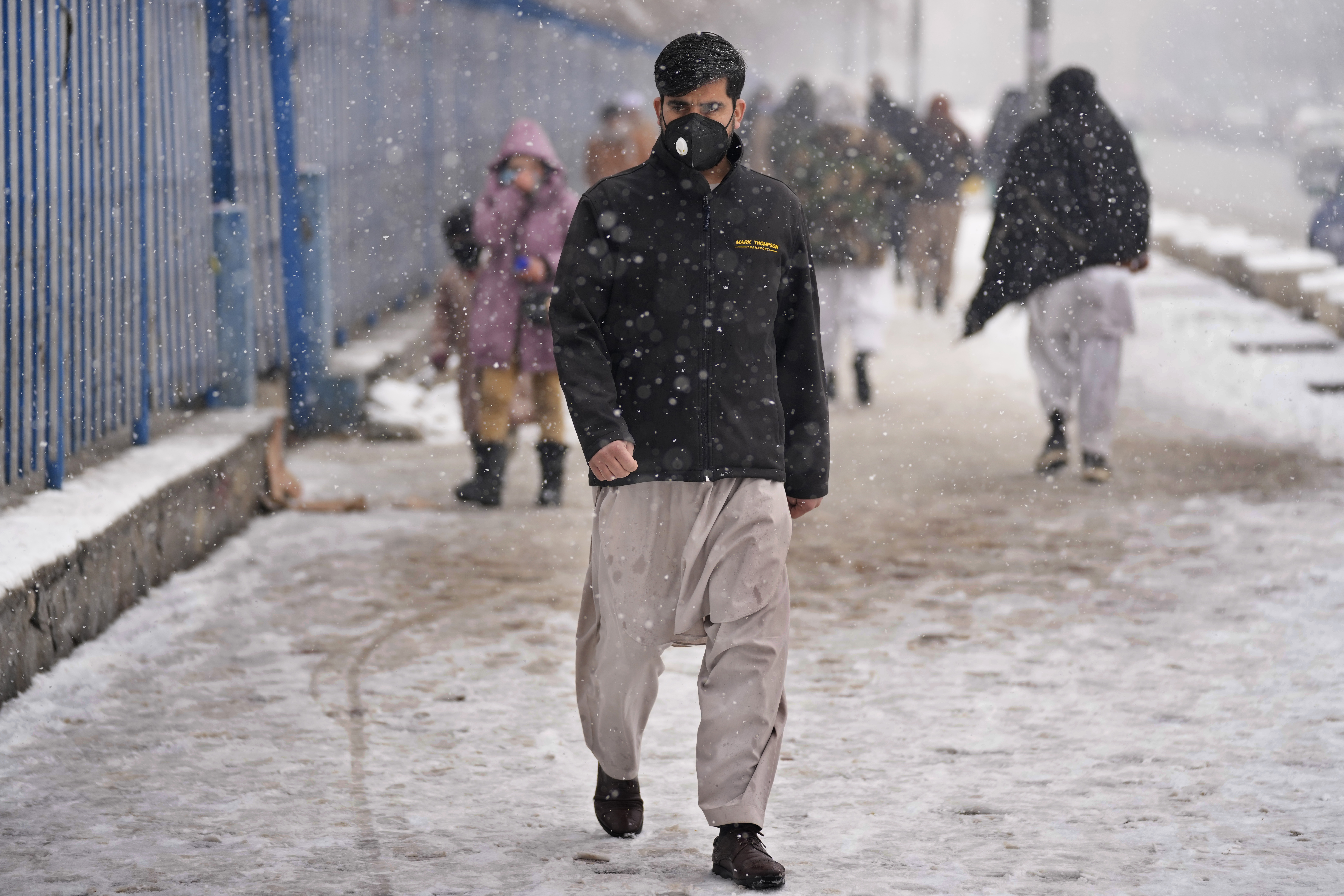 An Afghan man wears a mask to help curb the spread of COVID-19, as he walks in the snow, in Kabul