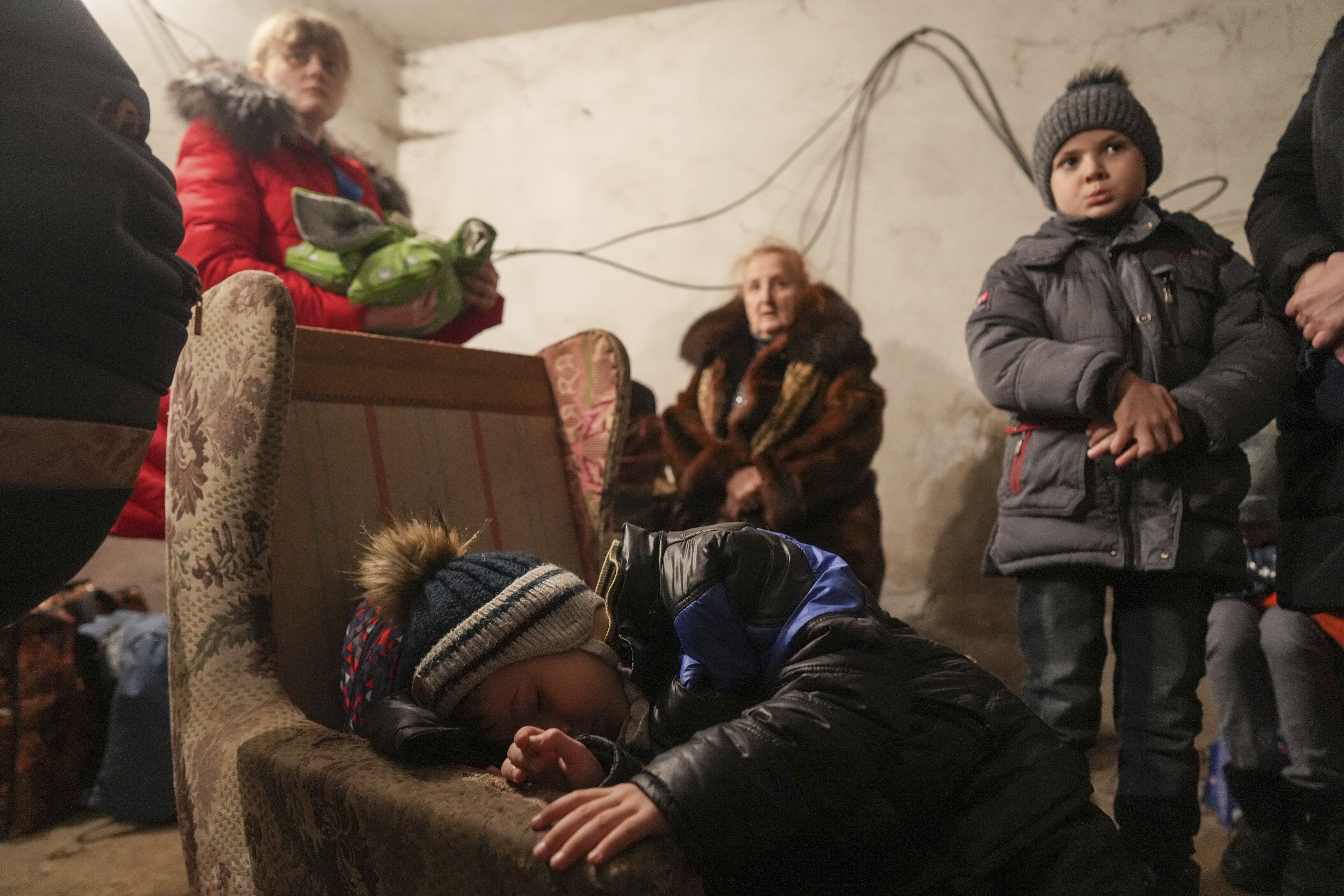 A child sleep in an armchair as other stand around in a shelter during Russian shelling, in Mariupol, Ukraine, Thursday, Feb. 24, 2022