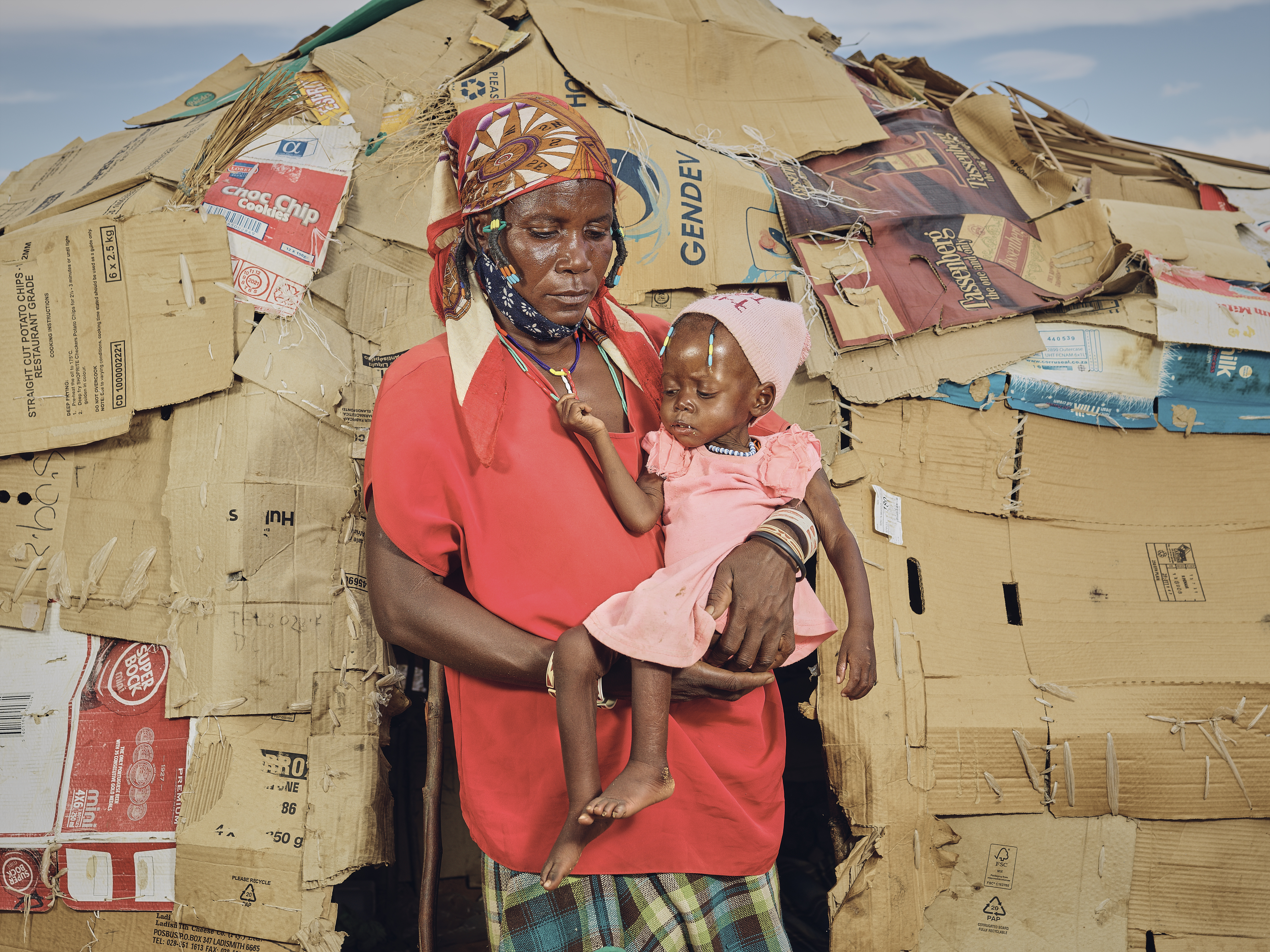 A photo of a woman standing outside a refugee camp, carrying a child.