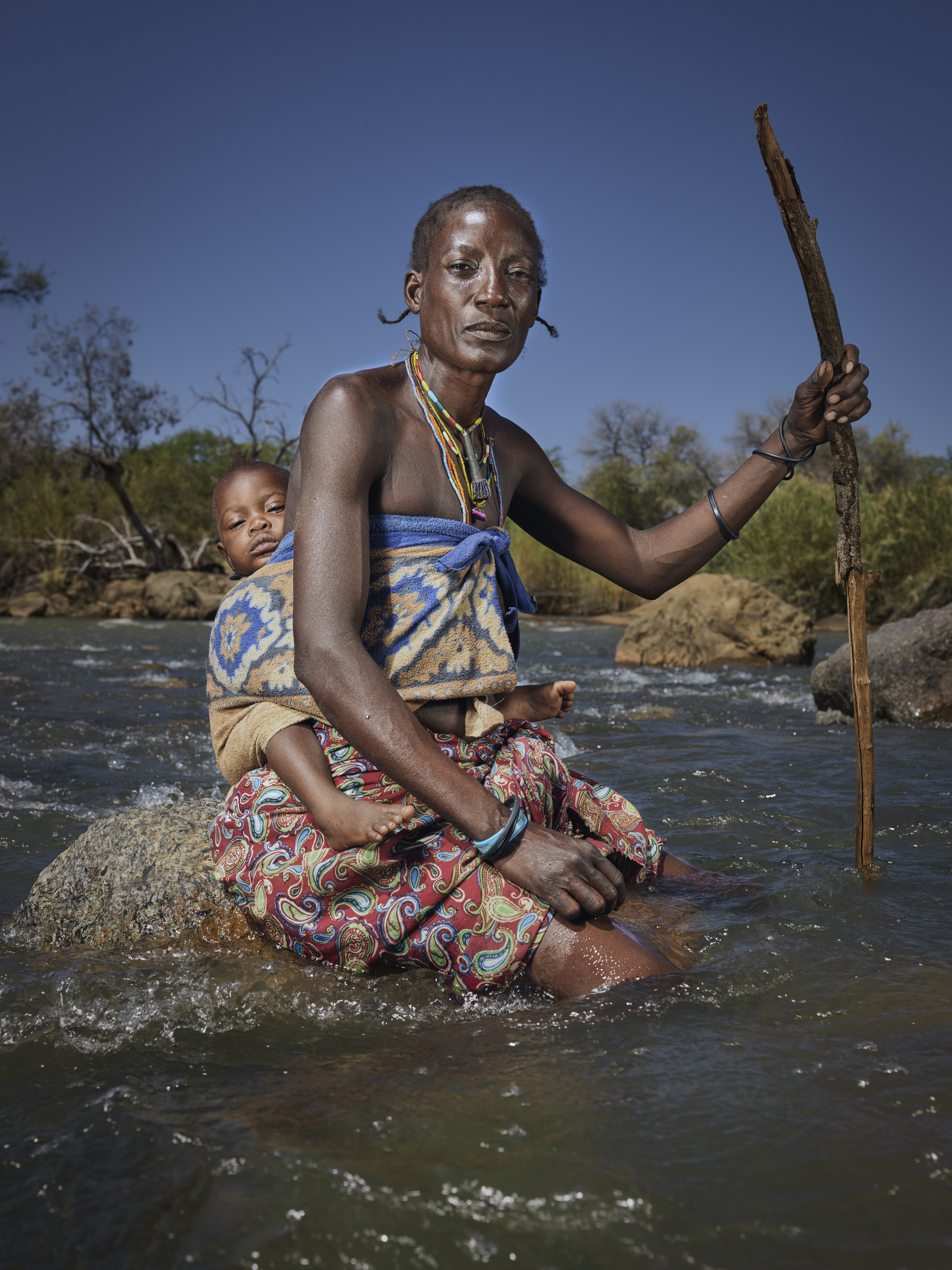 A photo of a woman with a child strapped to her back as they cross the river to get to Namibia from Angola.