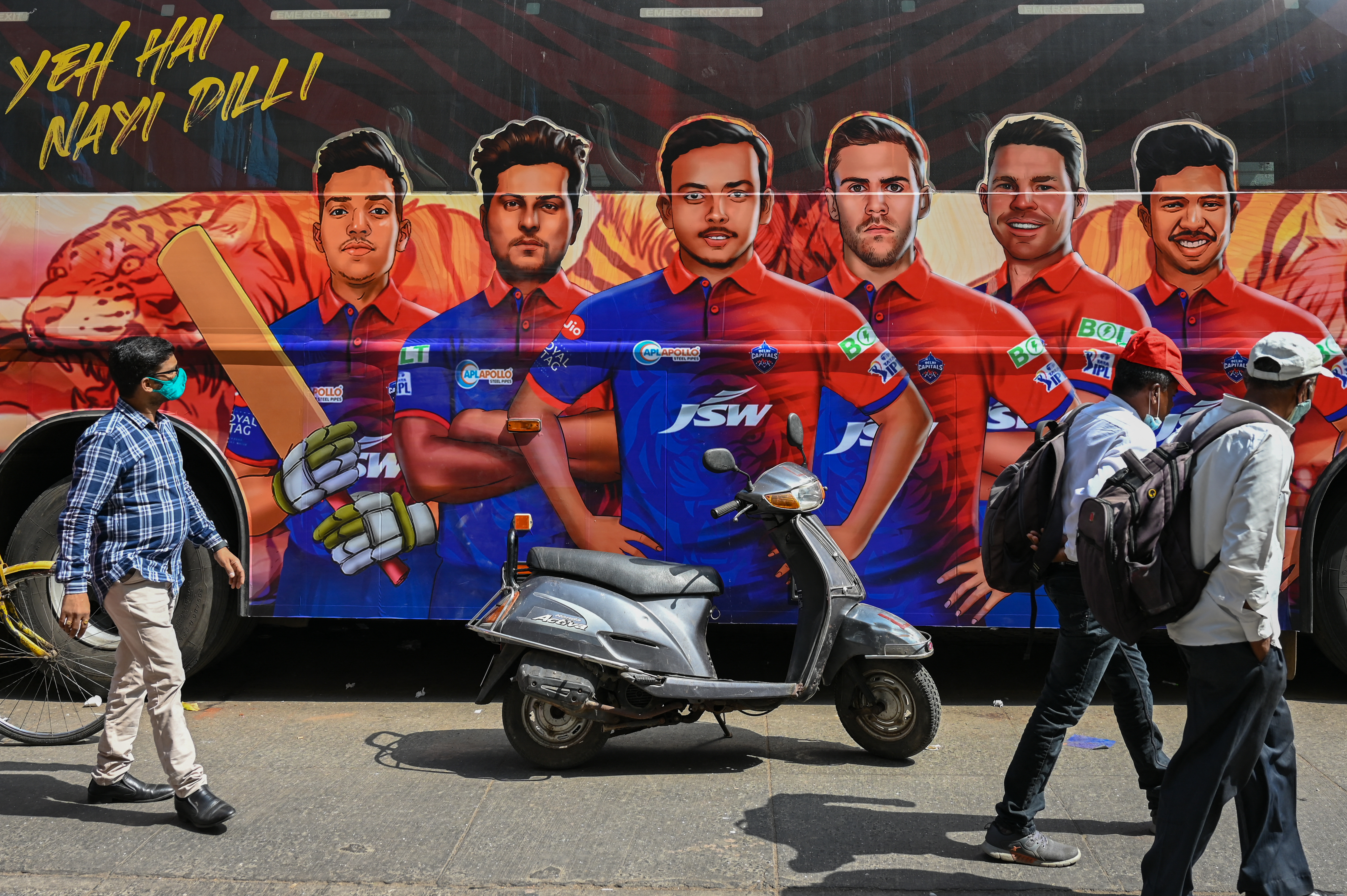 Pedestrians walk past the bus of Indian Premier League's (IPL) Delhi Capitals in Mumba
