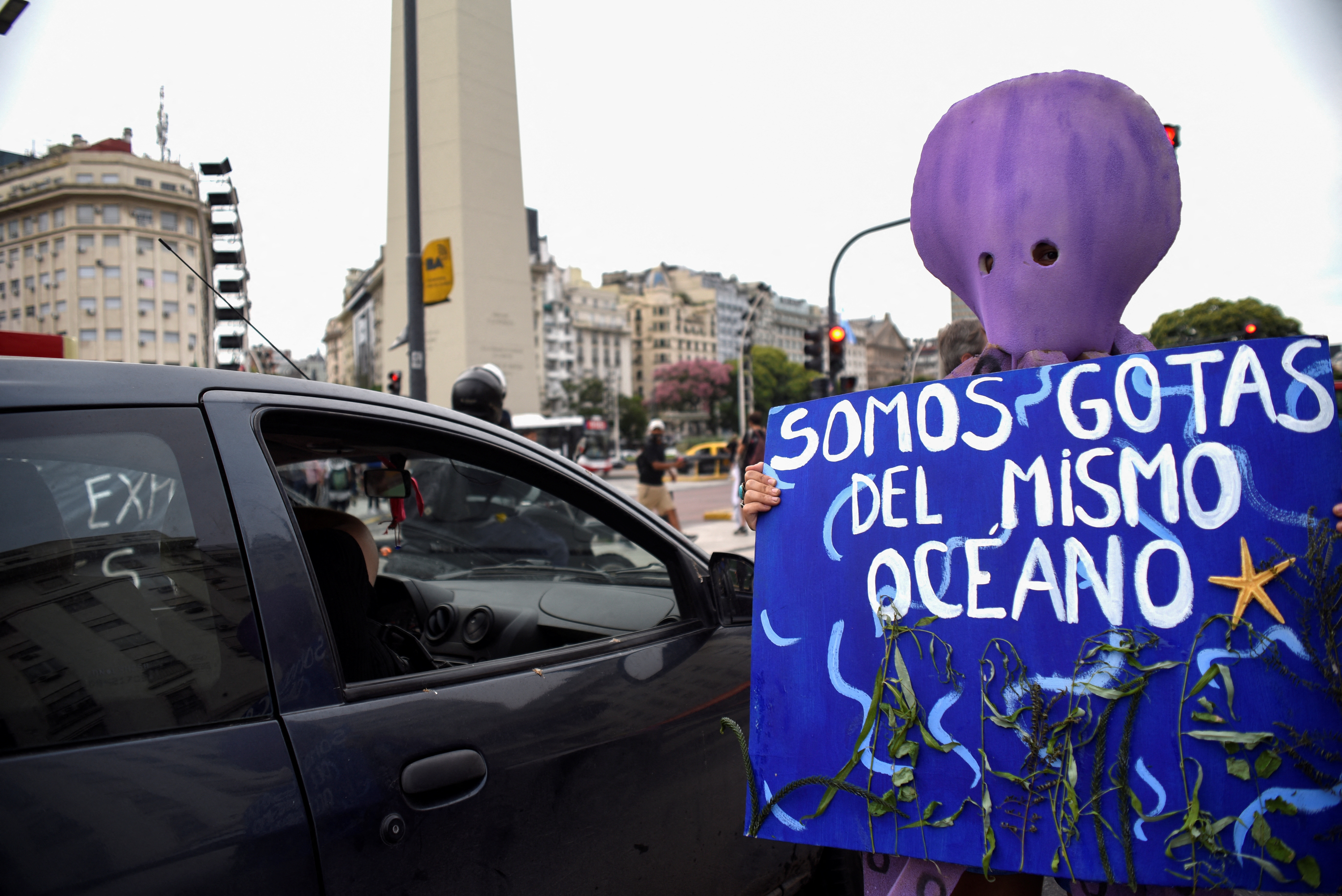 A demonstrator wearing an octopus mask holds a placard that reads 'We are drops of the same ocean'