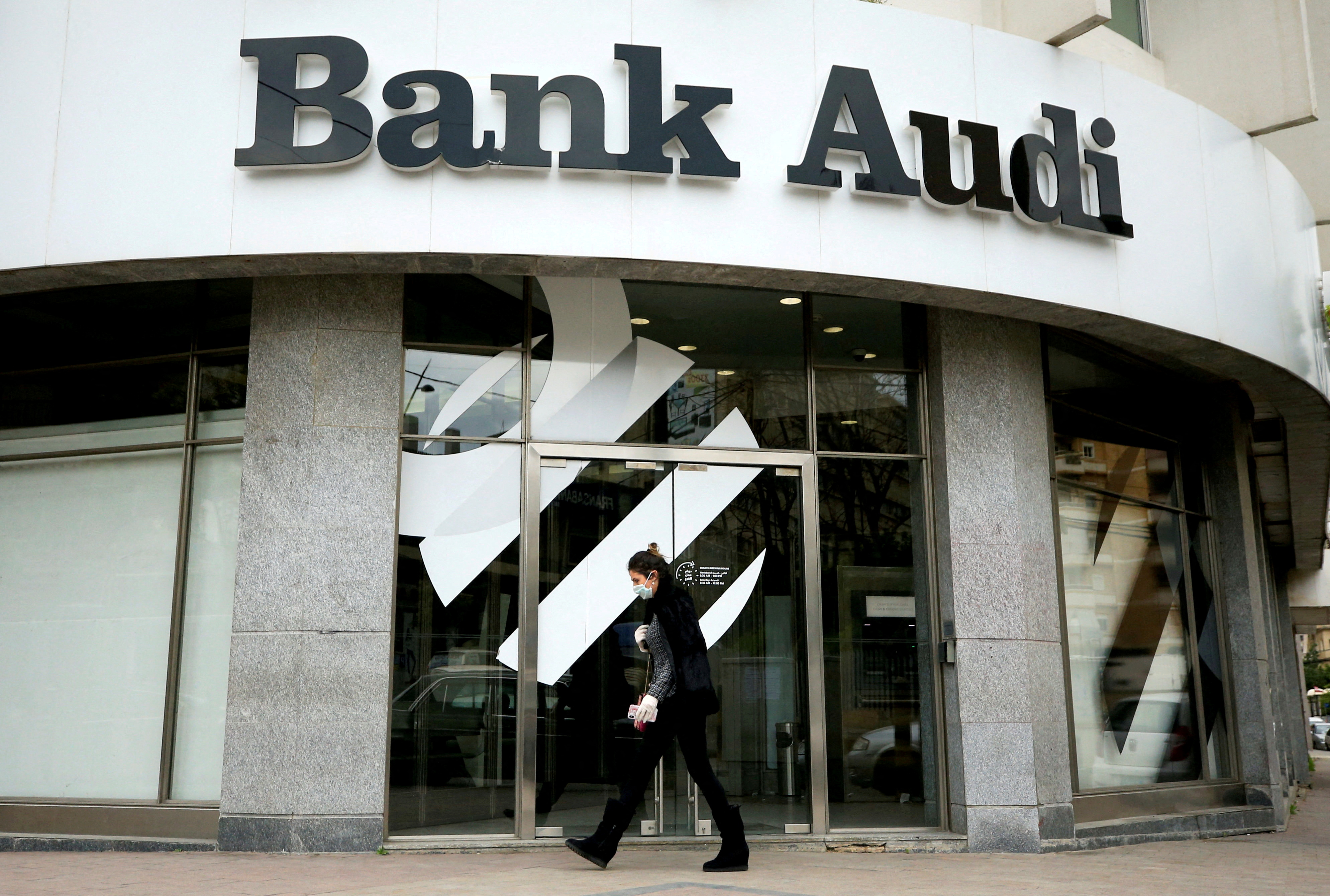A woman wearing a face mask walks by a closed branch of Bank Audi after Lebanon declared a state of emergency over the spread of the coronavirus, in Sidon, Lebanon, March 17, 2020.