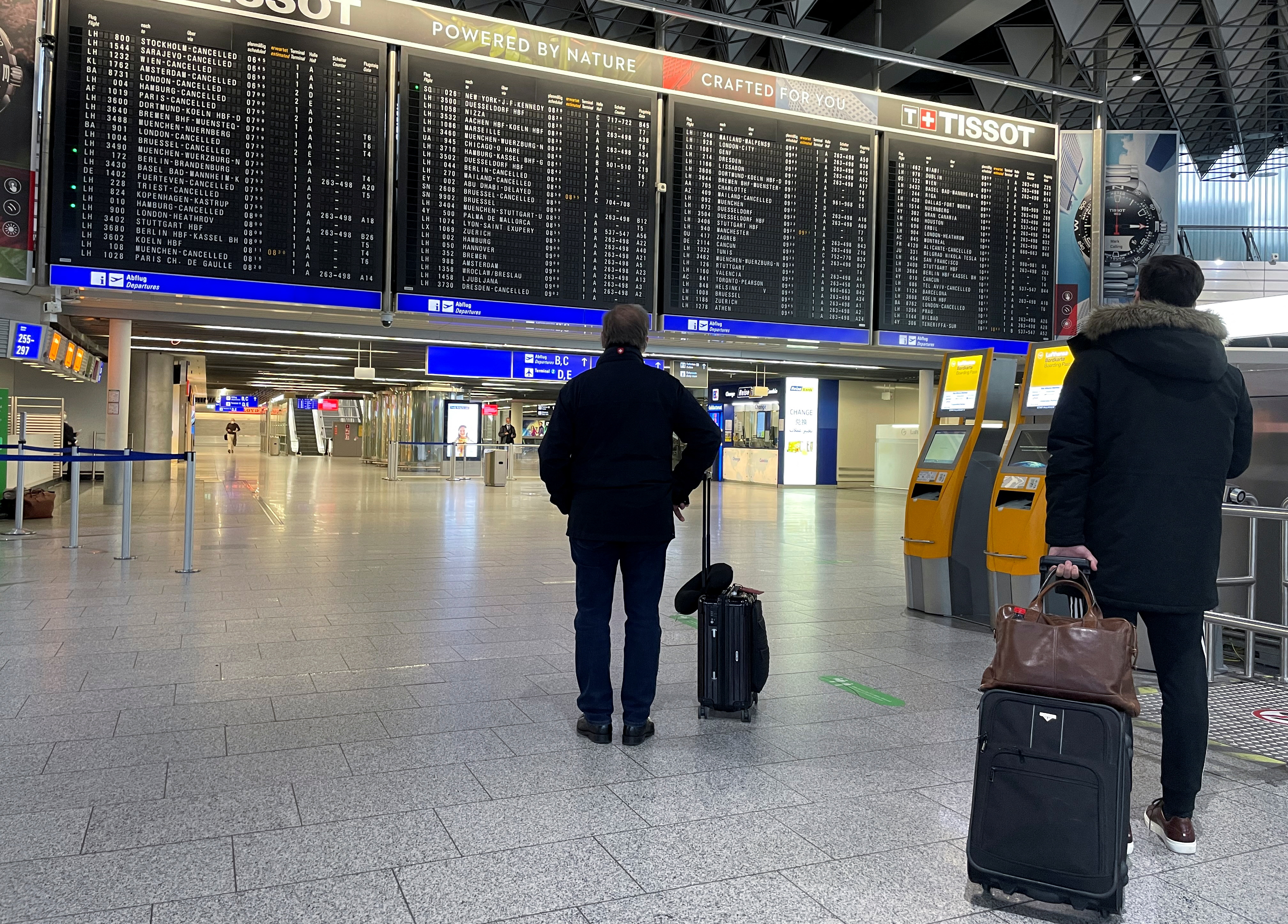 Passengers stand in front of a timetable showing many cancelled flights at Frankfurt Airport