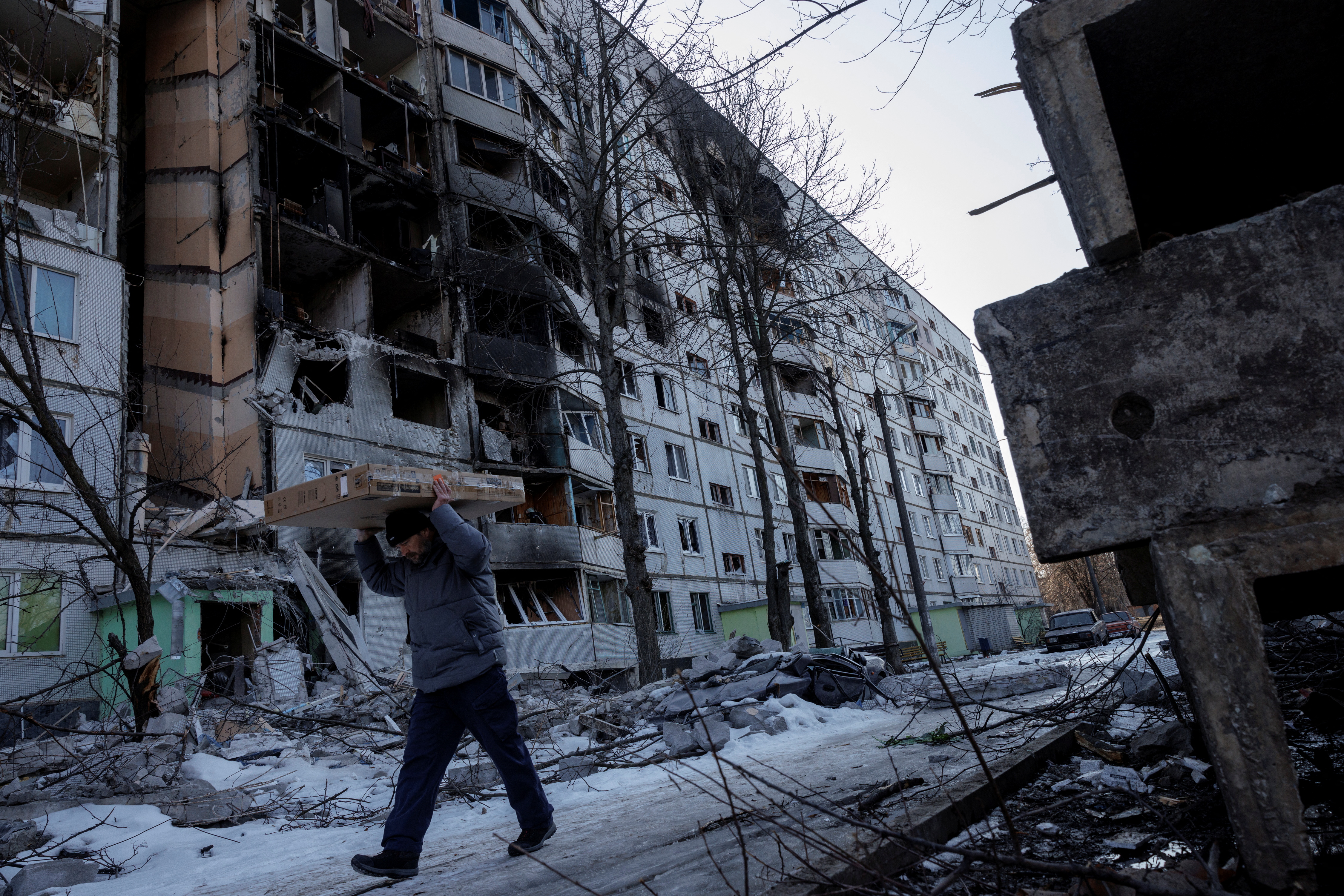 A man carries possessions out of a building hit by a bomb