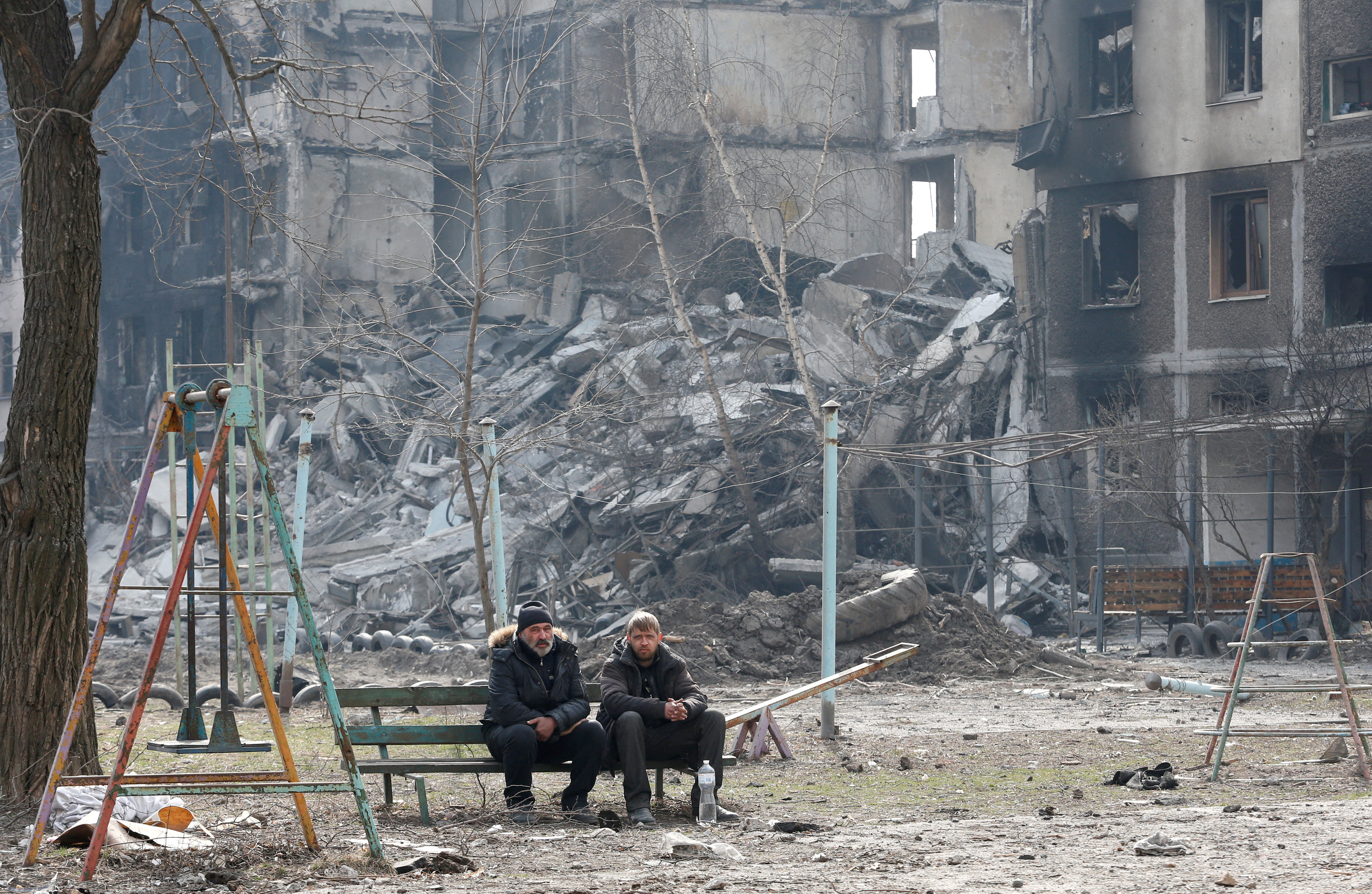 Local residents sit on a bench near an apartment building destroyed in the course of Ukraine-Russia conflict.