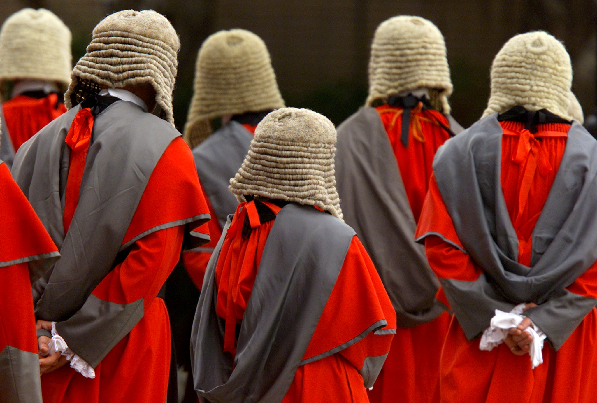 Supreme Court judges in red robes, grey over shoulder sashes and long, curled, horse hair wigs stand with their backs to their camera at the opening of Hong Kong's legal year