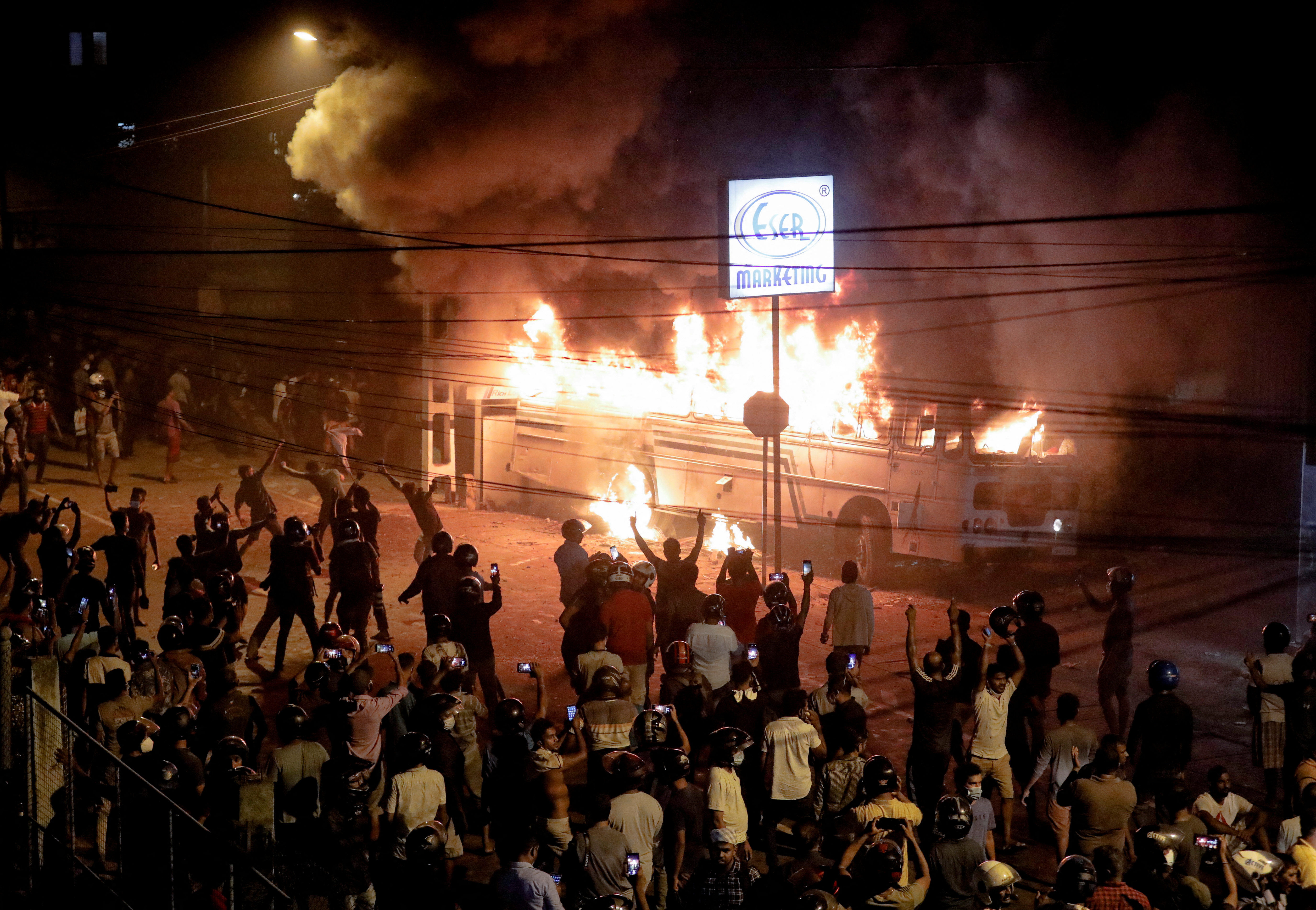 Demonstrators react after they set a fire to a bus parked at the top the road to Sri Lankan President Gotabaya Rajapaksa's residence during a protest against him