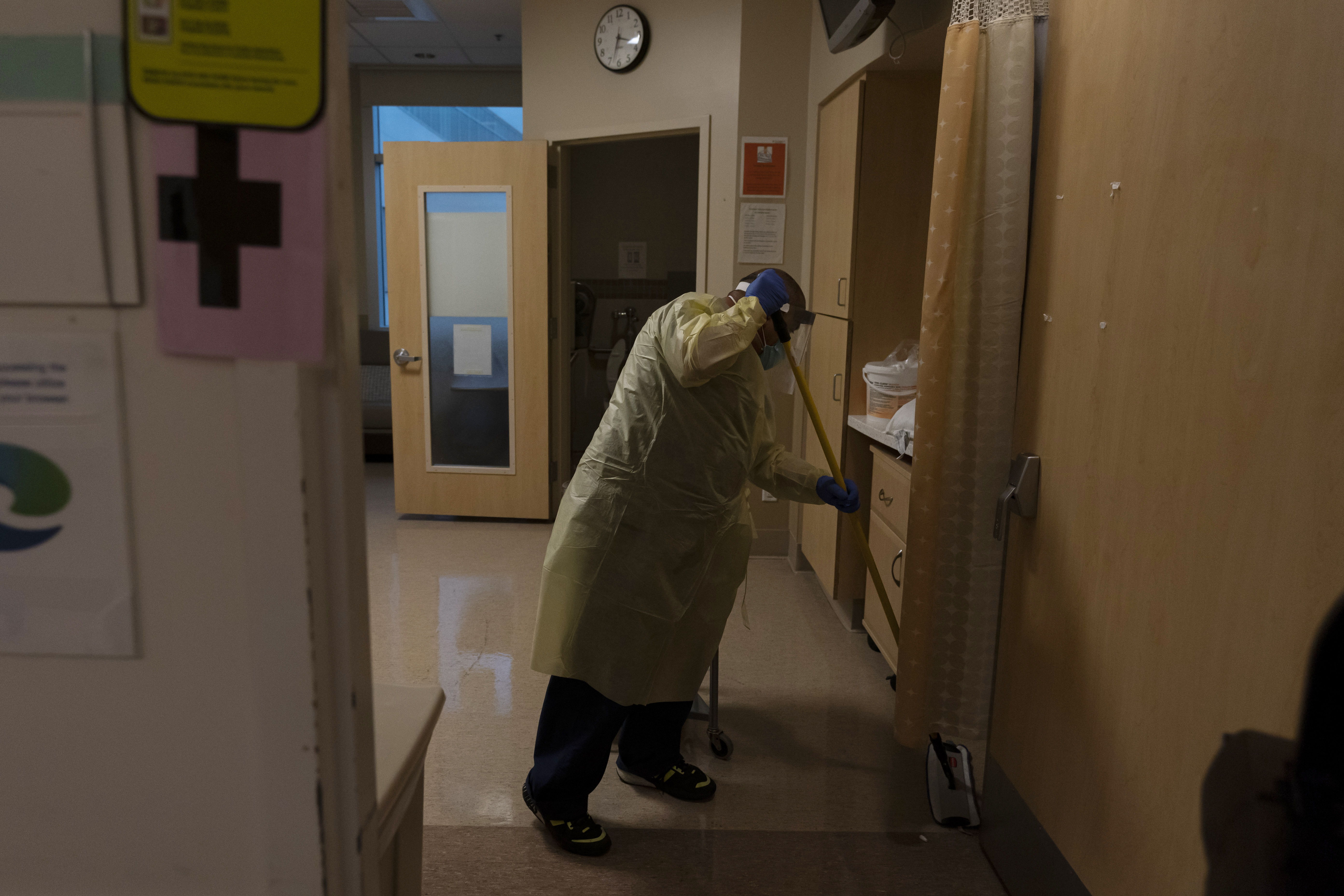 FILE - Environmental technician Gerardo Velazquez cleans a room after a COVID-19 patient was transferred to an intensive care unit at Providence Holy Cross Medical Center in Los Angeles, Monday, Dec. 13, 2021. The worldwide surge in coronavirus cases driven by the new omicron variant is the latest blow to already strained hospitals, nursing homes, police departments and supermarkets struggling to maintain a full contingent of nurses, police officers and other essential workers as the pandemic enters its third year. 