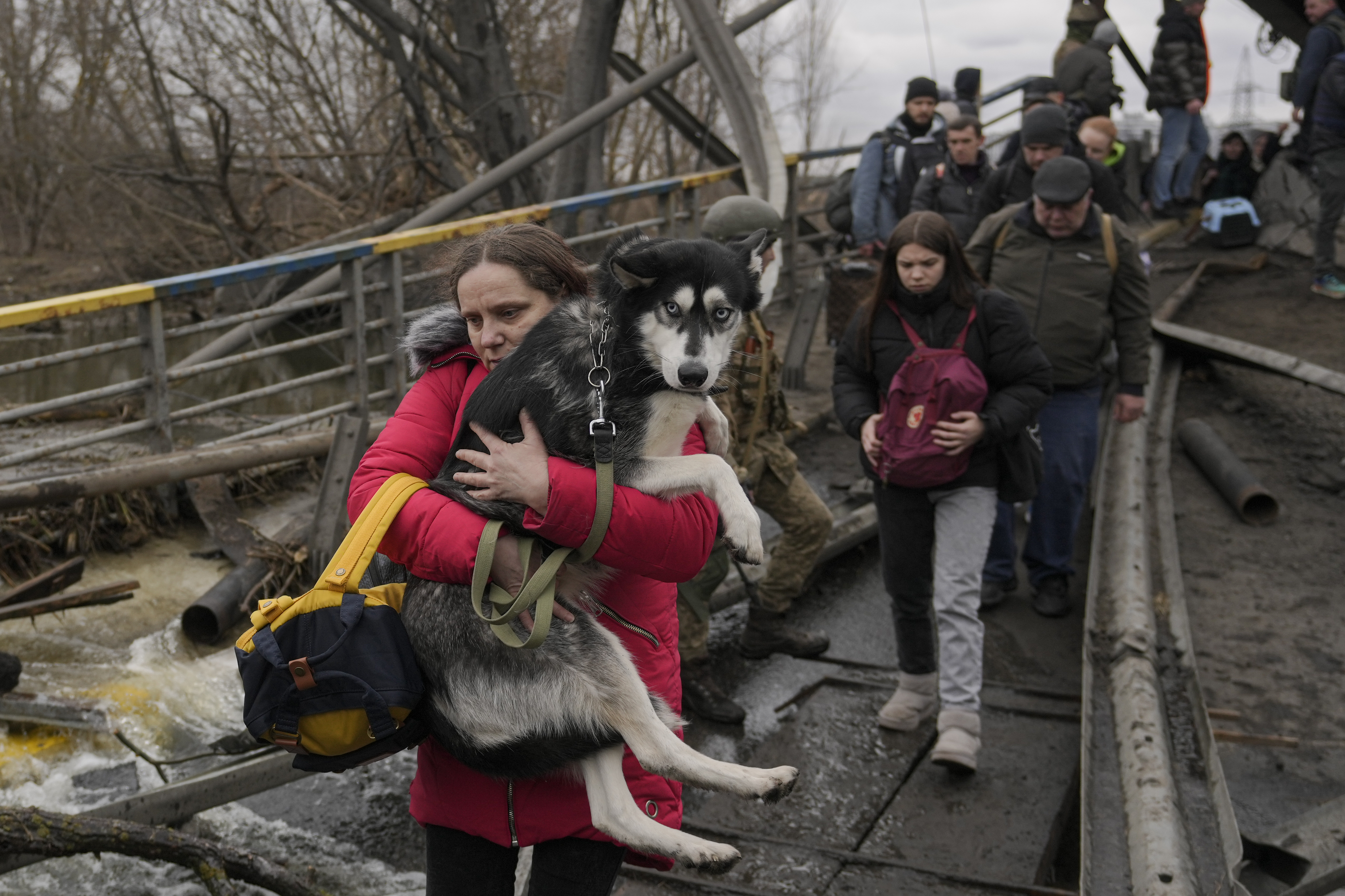 A woman holds a dog while crossing the Irpin River on an improvised path under a bridge that was destroyed by a Russian airstrike