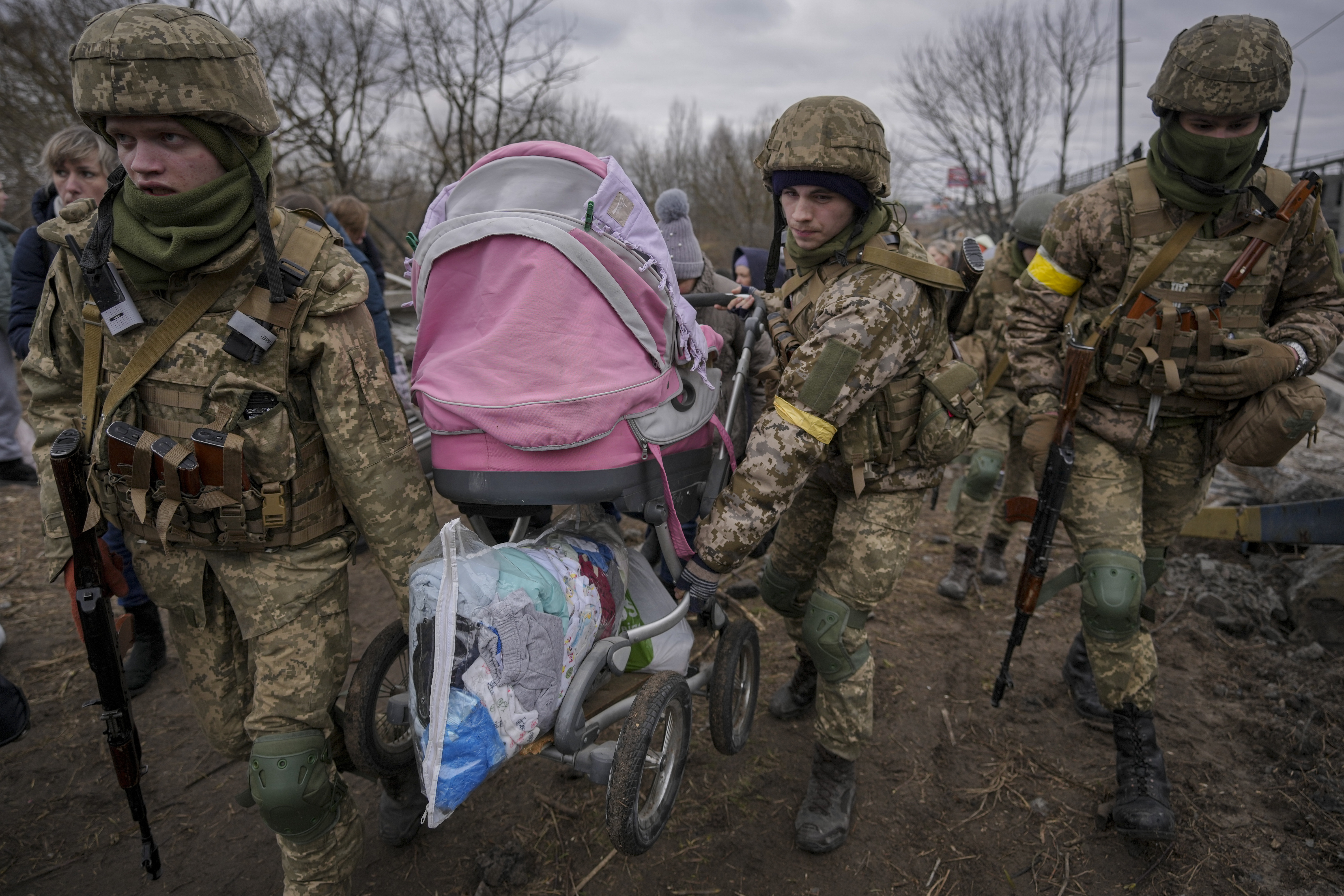 Ukrainian servicemen carry a baby stroller after crossing the Irpin River on an improvised path under a bridge that was destroyed by a Russian airstrike