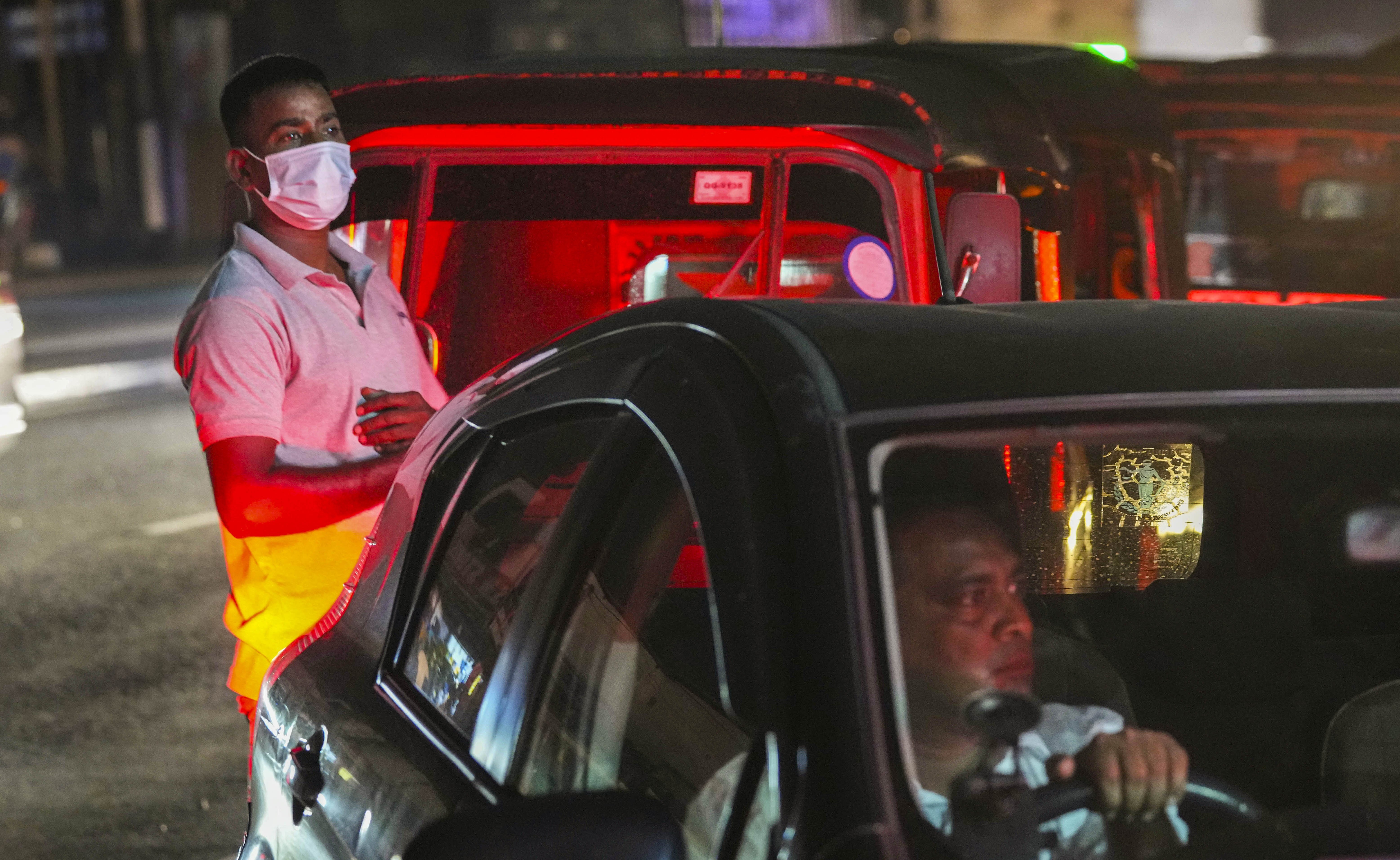A Sri Lankan auto rickshaw driver, left, and other motorists queue up for fuel along a road near a fuel pump during a power cut