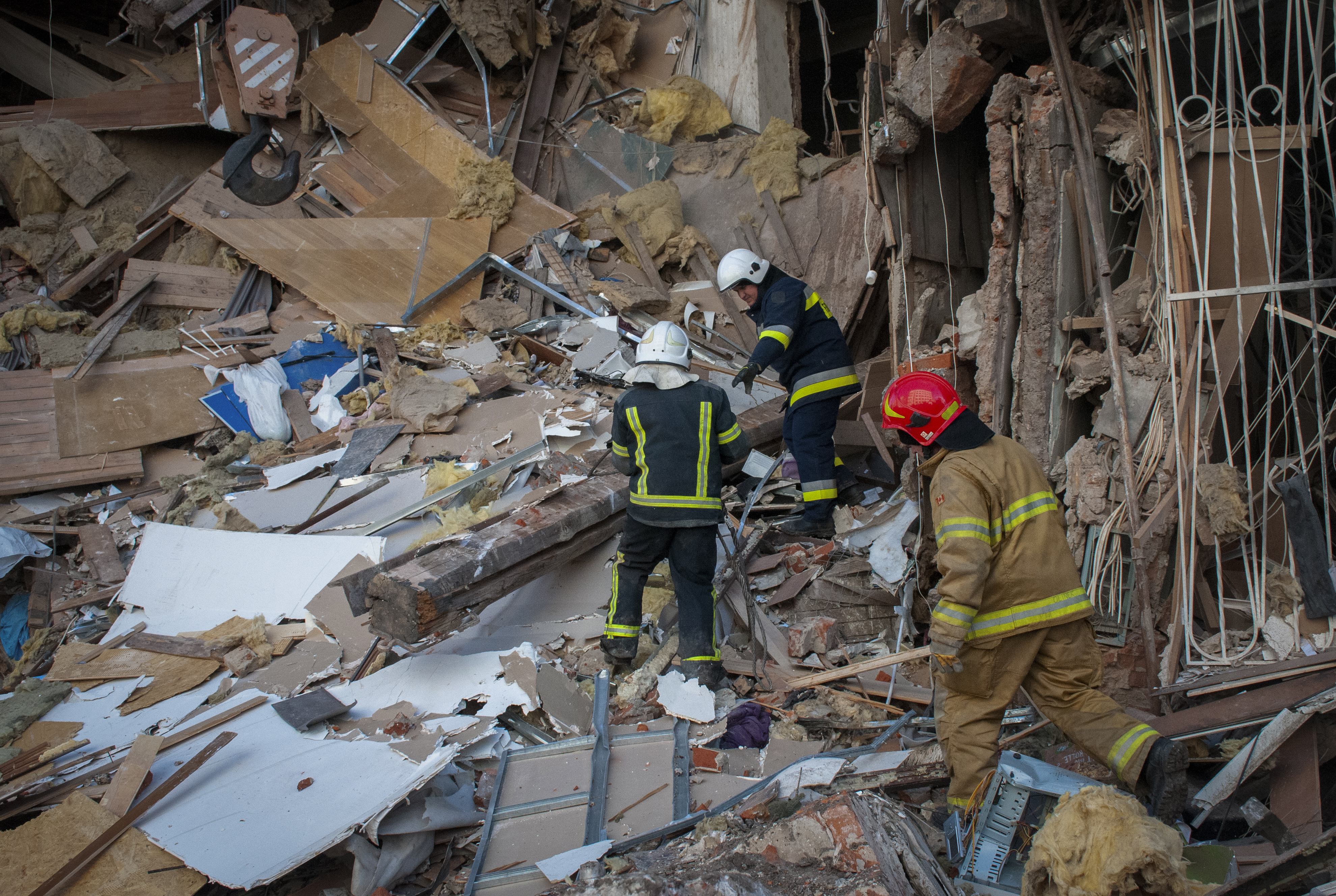 Ukrainian firefighters work by a destroyed apartment building in Kharkiv