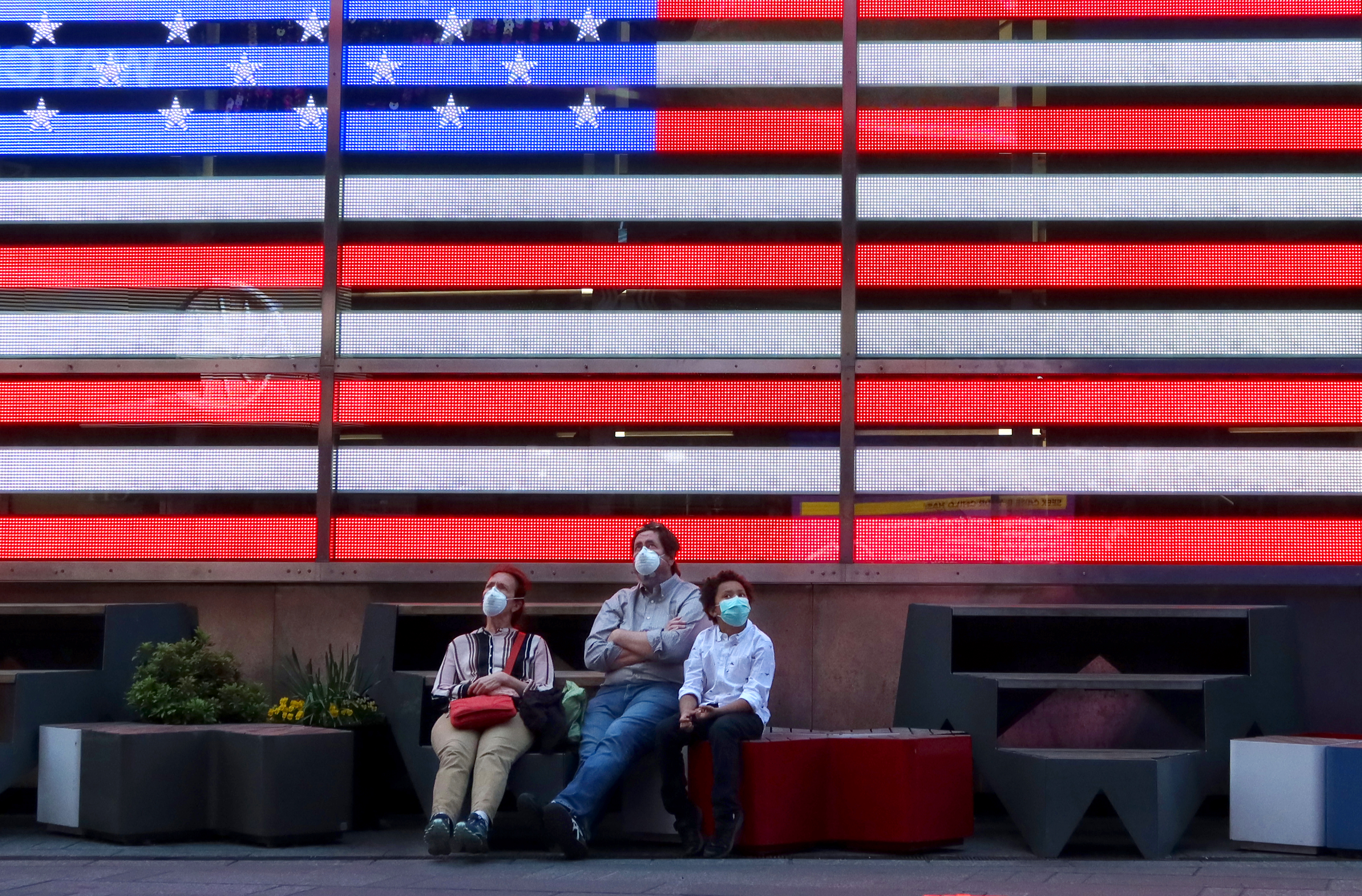 People in masks sit beneath an American flag
