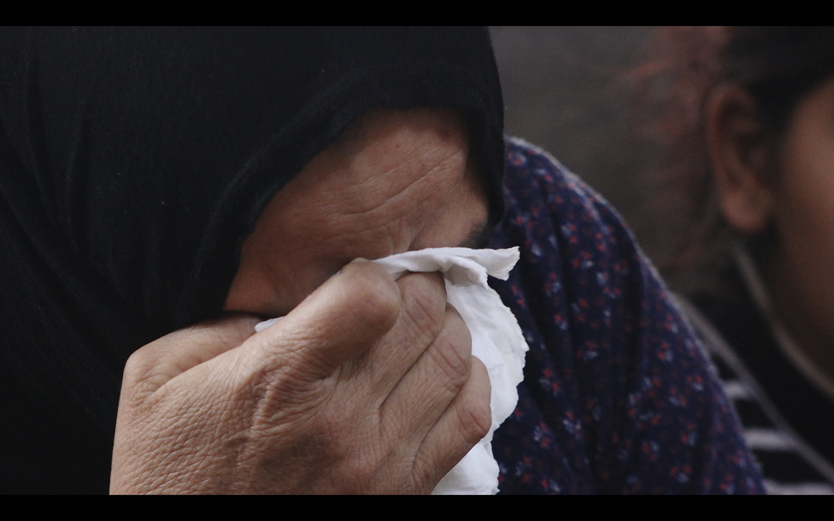 A woman wearing a black headscarf cries into a tissue