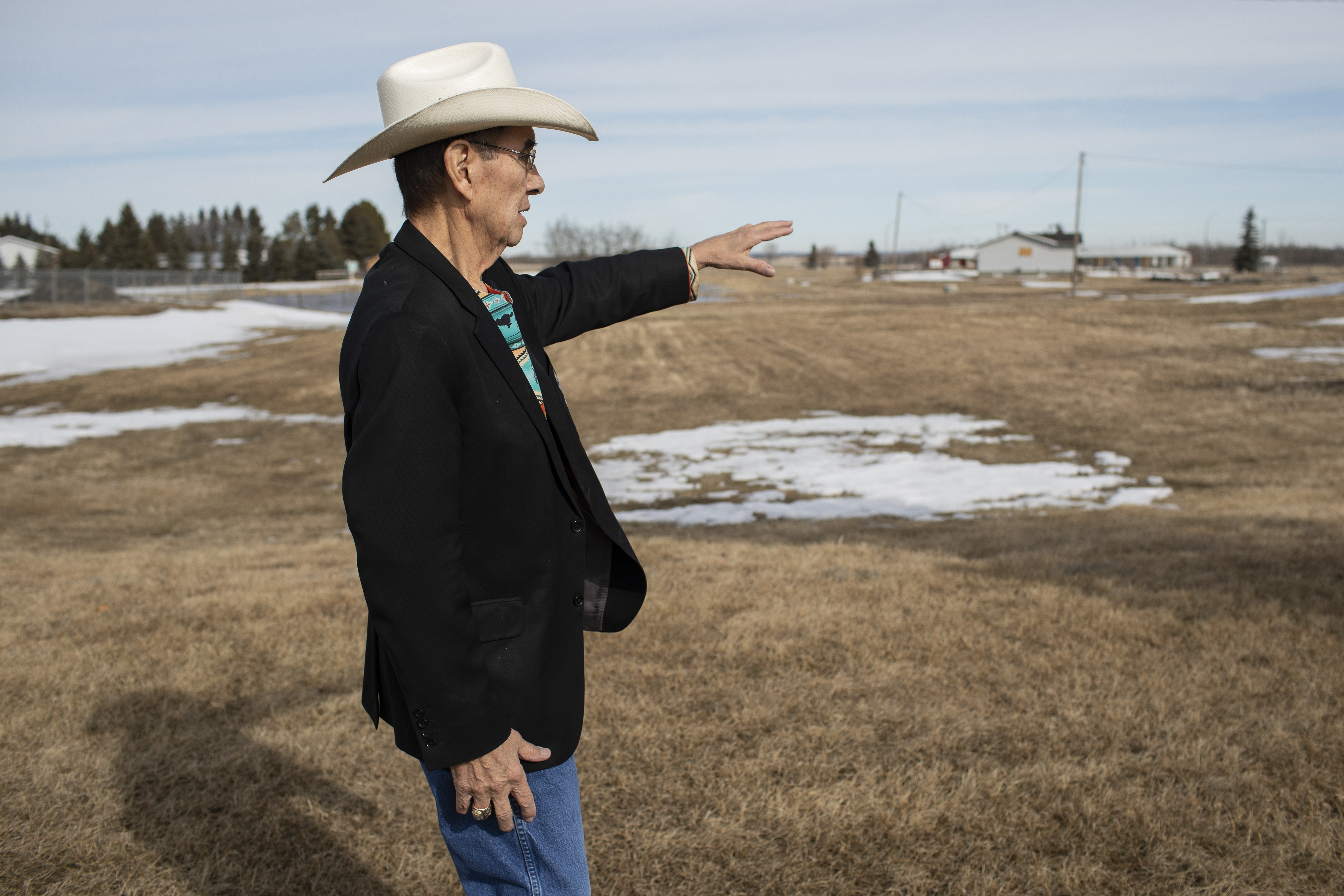 A photo of Chief Willie Littlechild pointing towards the distance in a field.