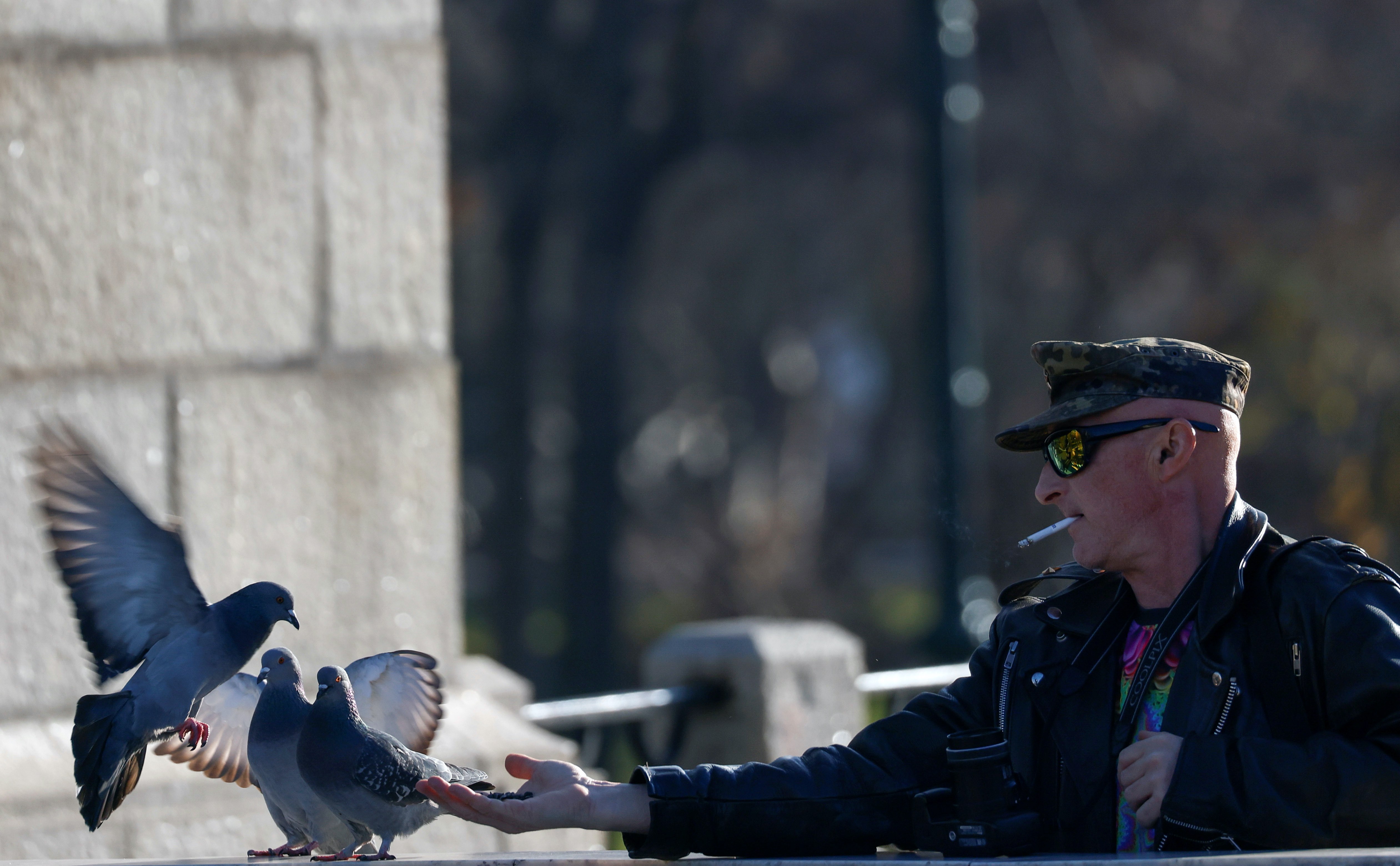 A man smokes a cigarette while feeding pigeons on a sunny day in Moscow, Russia