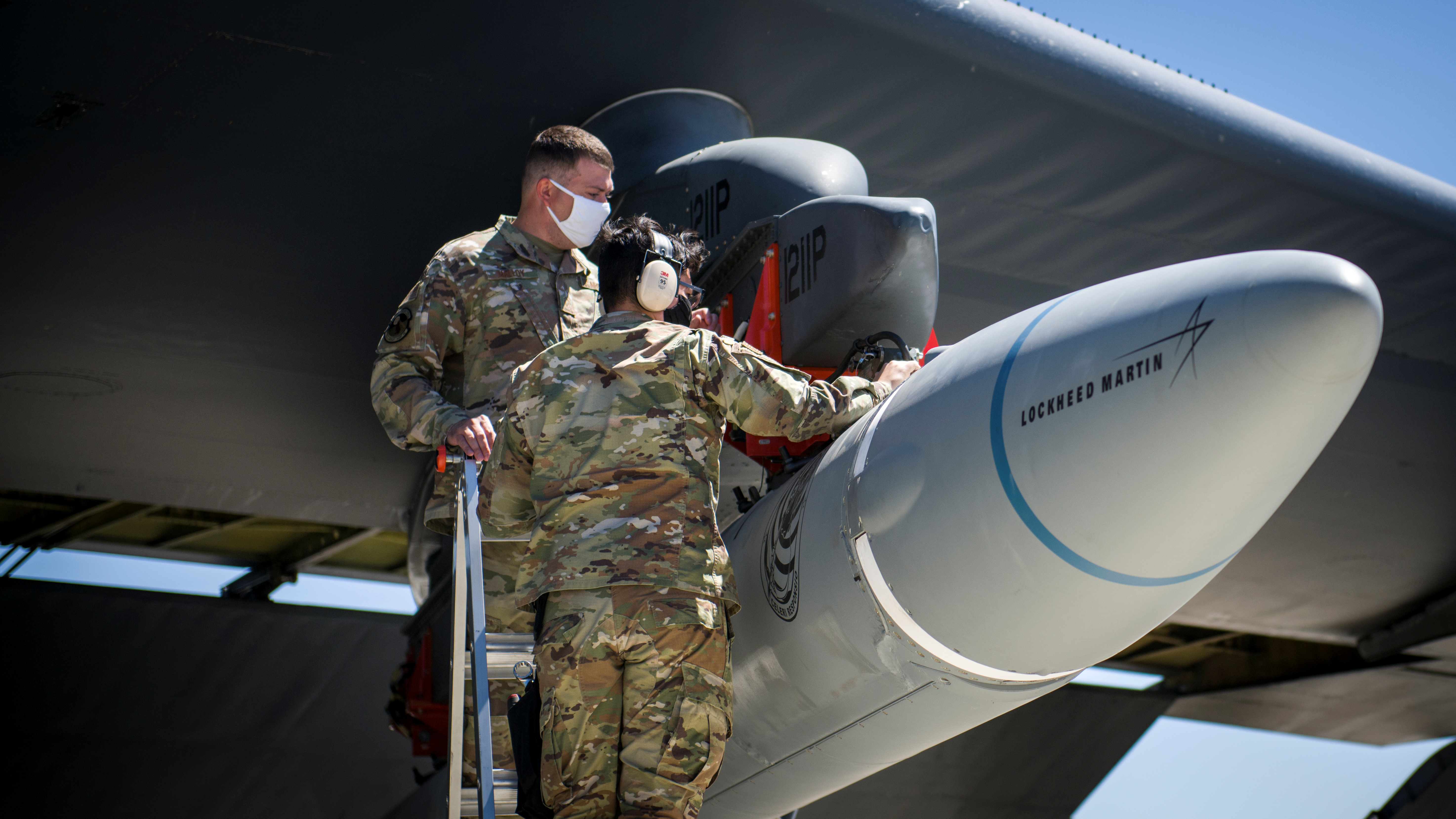 Two US servicemen adjust a hypersonic weapon beneath the wing of a B52 ahead of a test