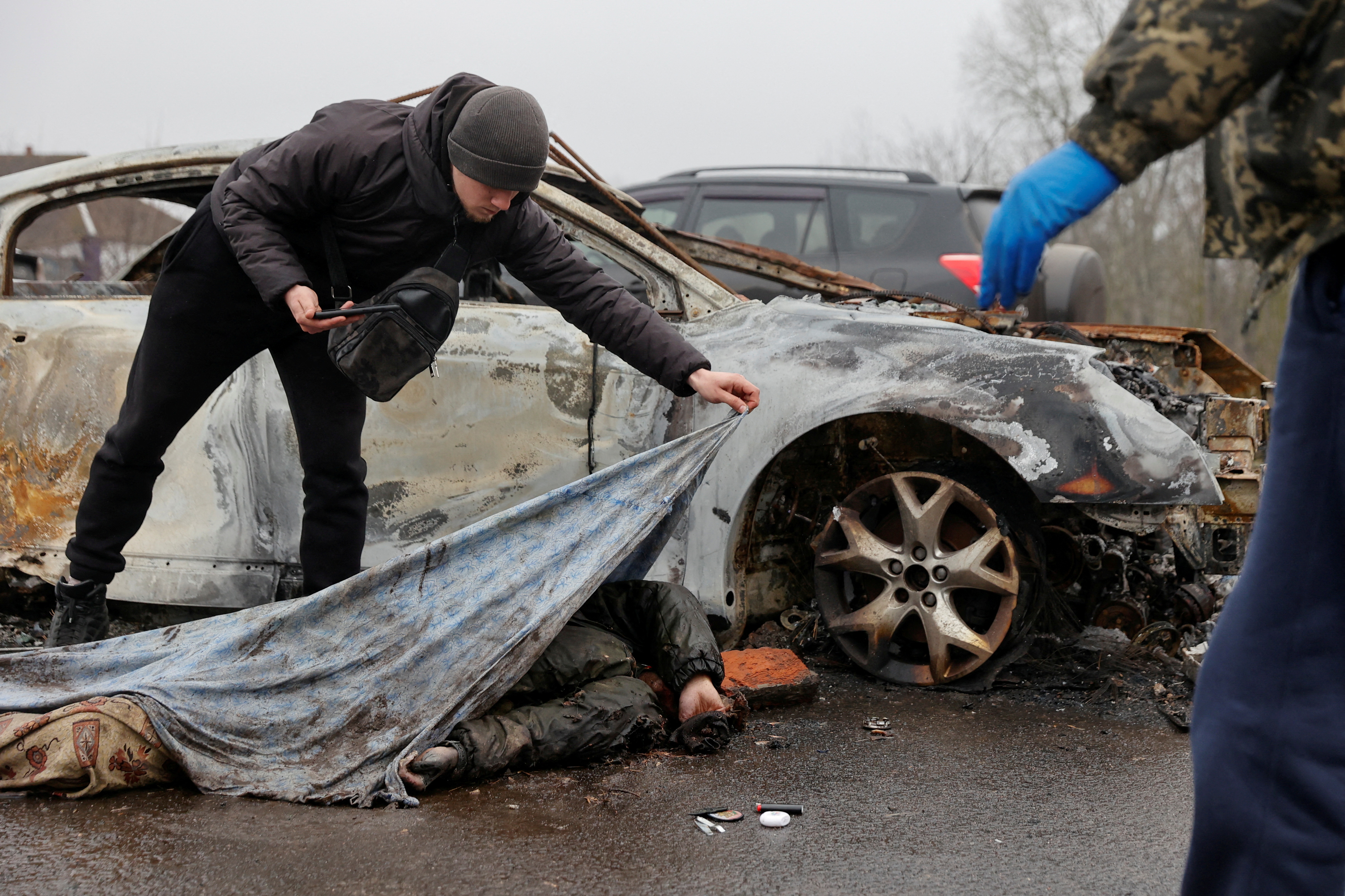 A worker of a funeral service uncovers a body of killed civilian, as Russia's attack on Ukraine continues, in the village of Nova Basan, in Chernihiv region, Ukraine April 1, 2022.