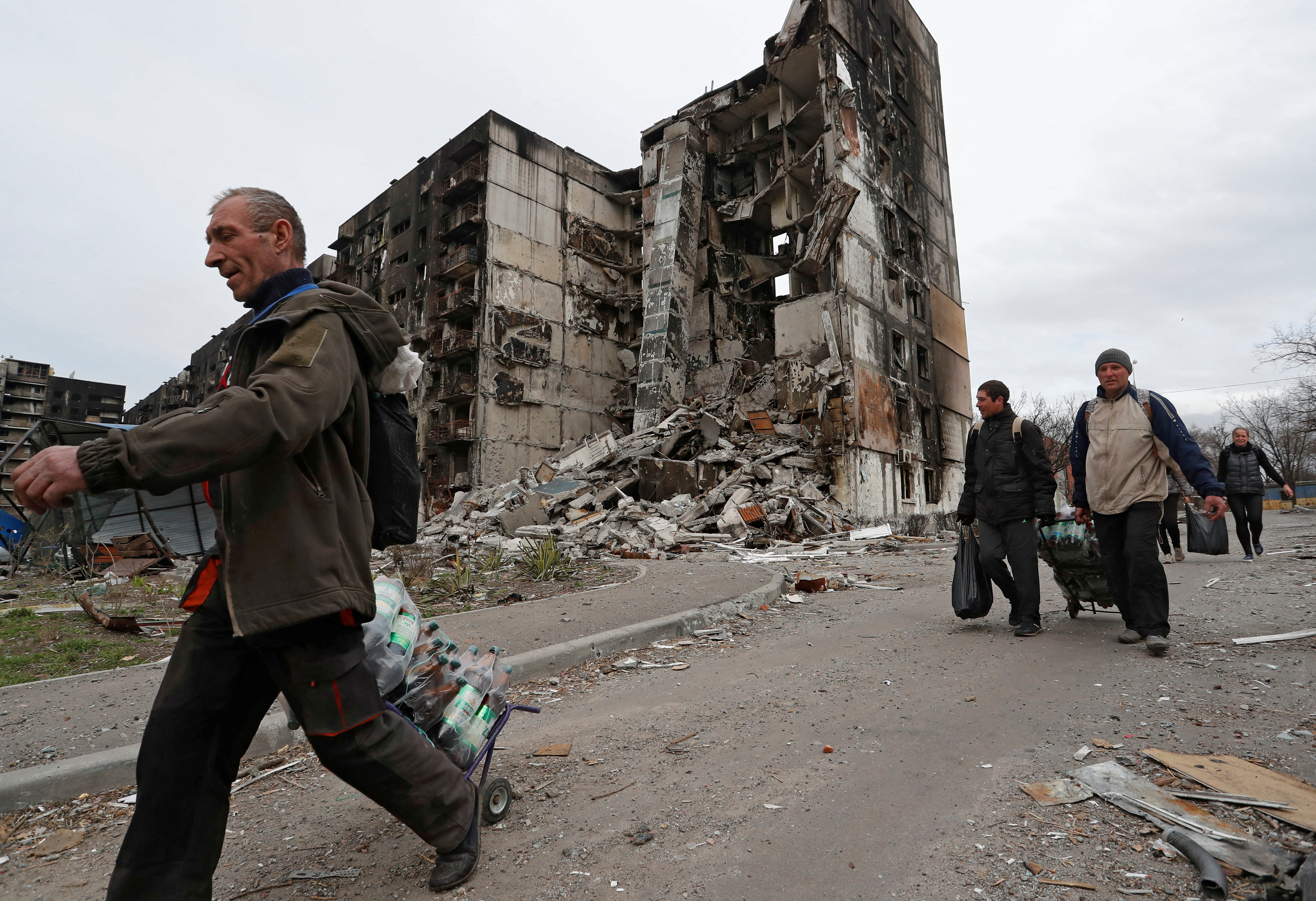 Local residents walk past a building destroyed during Ukraine-Russia conflict in the southern port city of Mariupol,