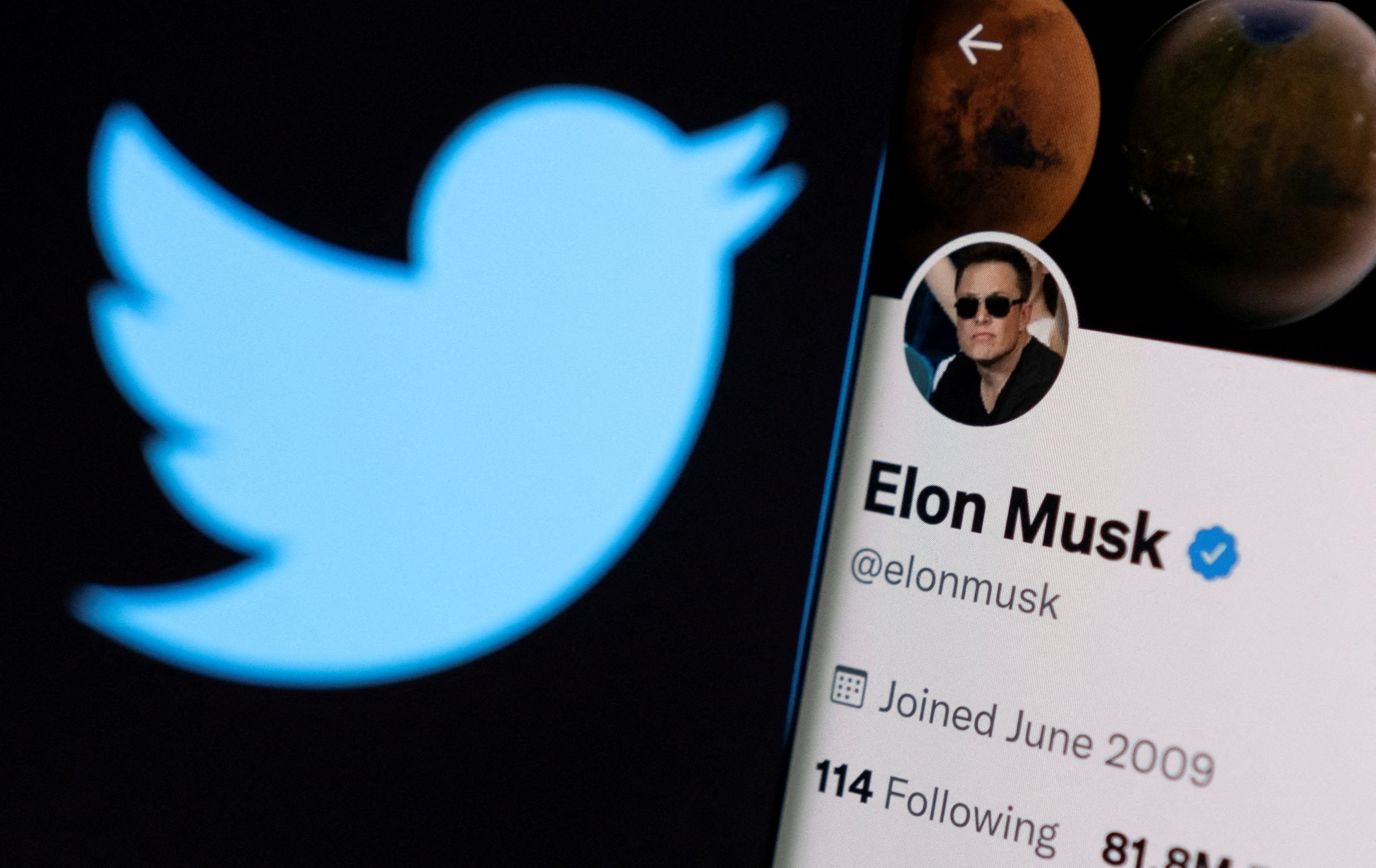 Elon Musk's twitter account is seen on a smartphone in front of the Twitter logo in this photo illustration taken