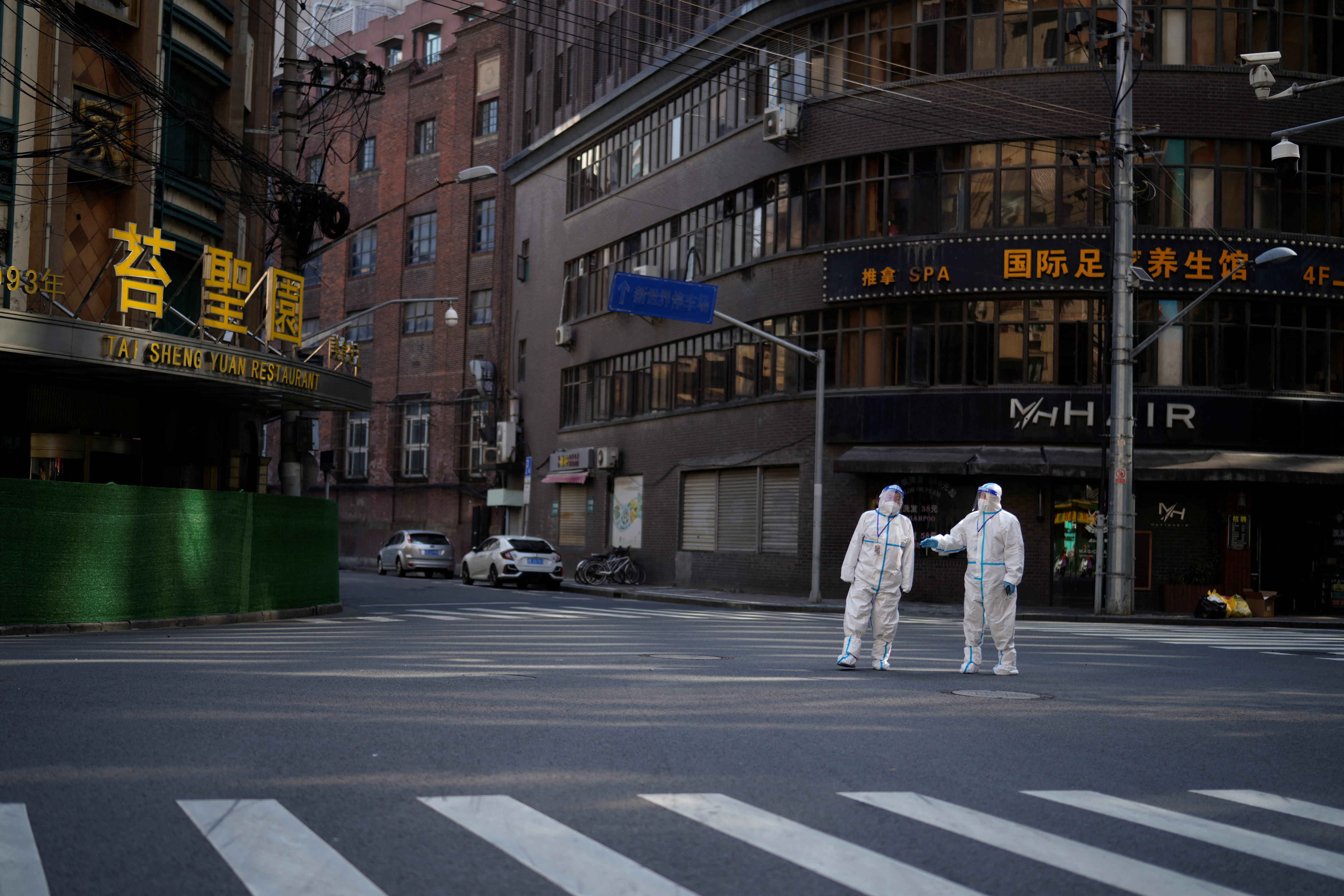 Workers in protective suits keep watch on a street during a lockdown in Shanghai