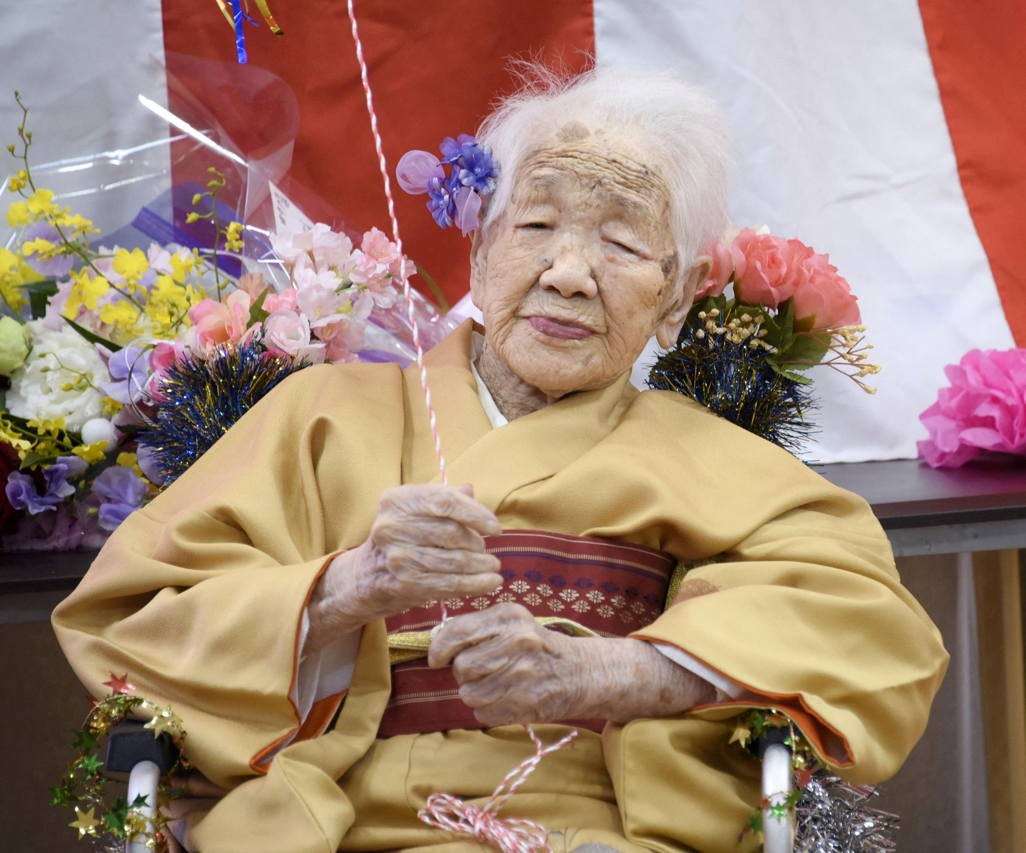 Kane Tanaka, wearing a traditional kimono in yellow, and surrounded by flowers pictured celebrating her 117th birthday