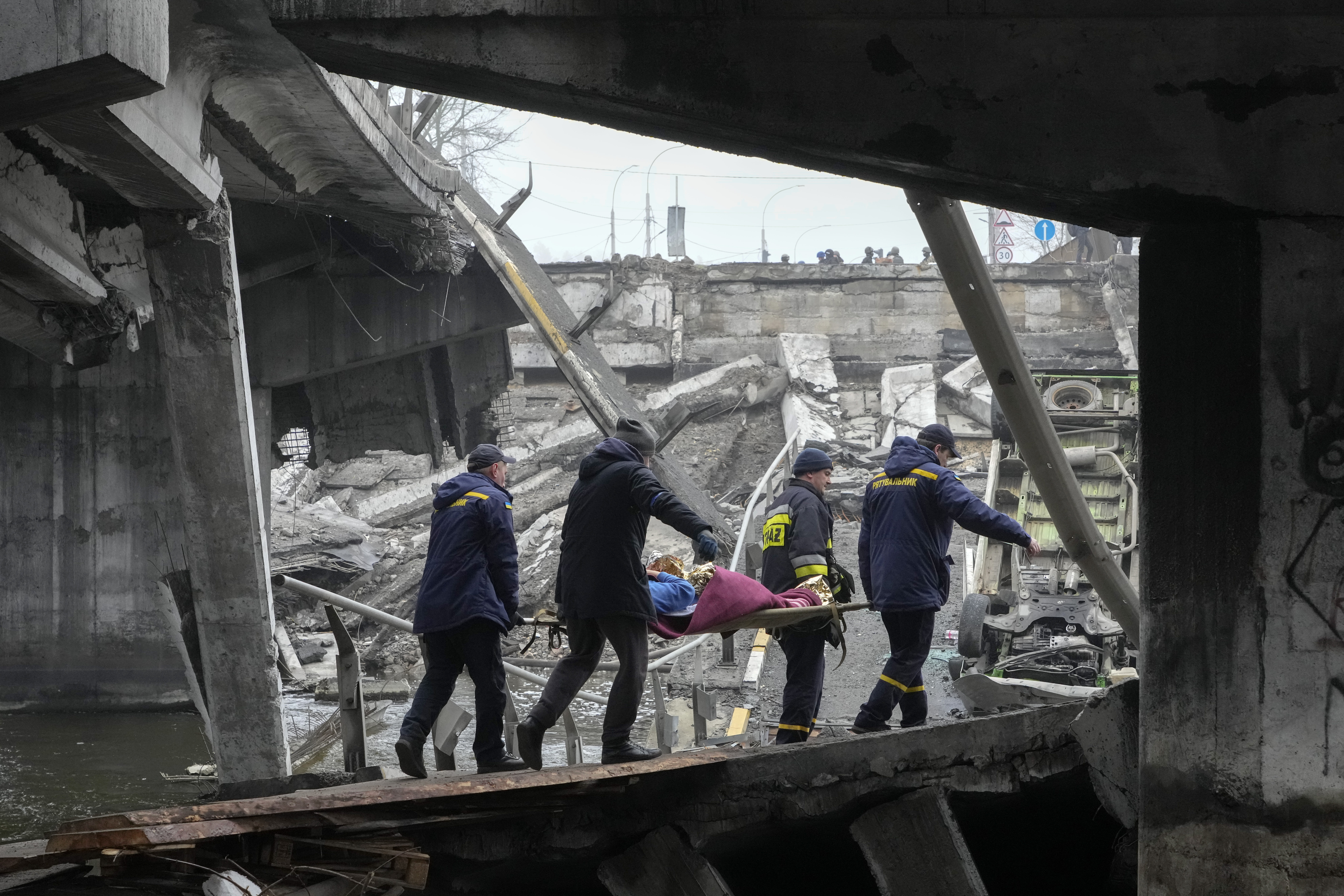 Rescue workers evacuate an elderly woman among destroyed buildings in Irpin