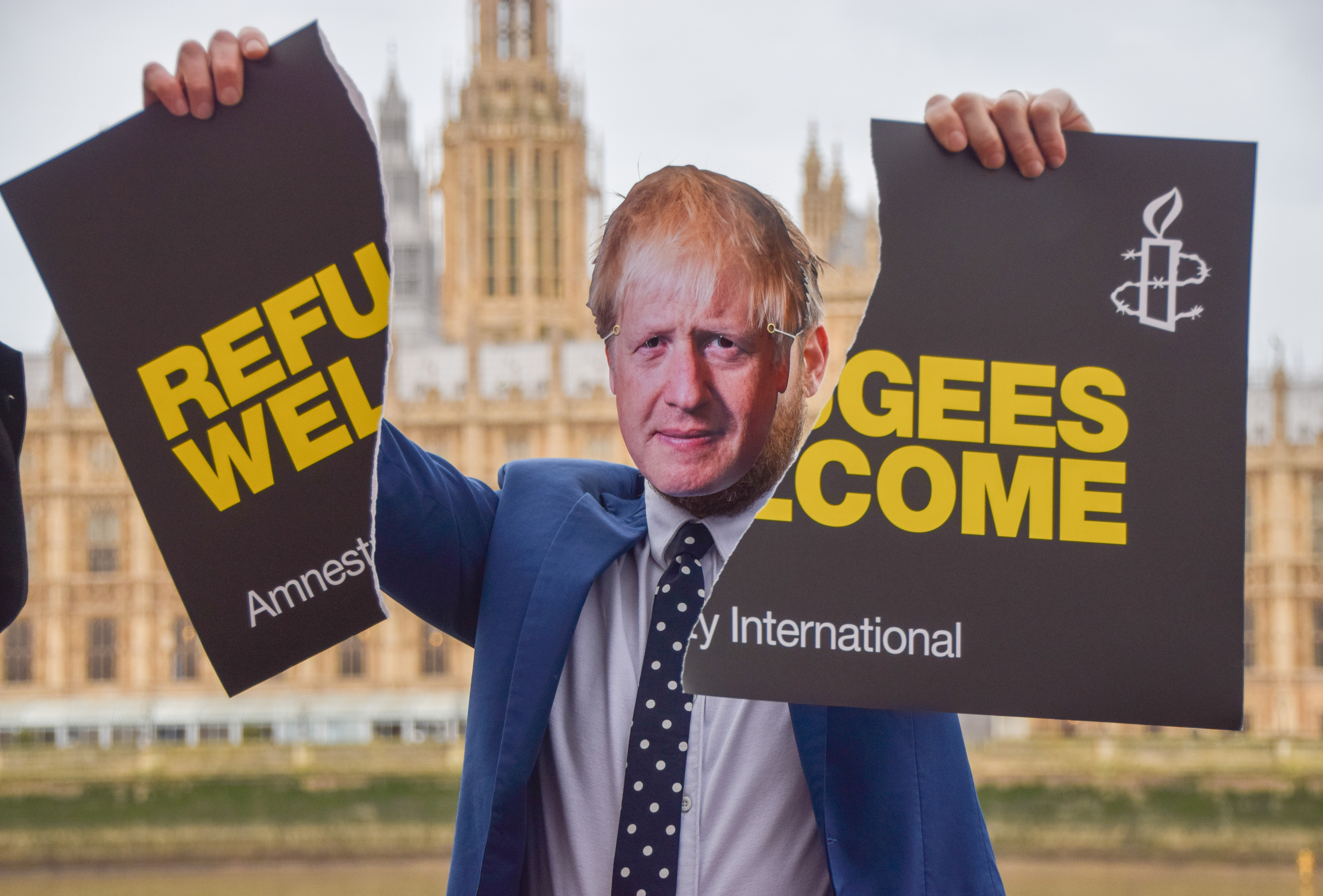 An activist dressed as Boris Johnson holds a torn 'Refugees Welcome' placard during the demonstration.