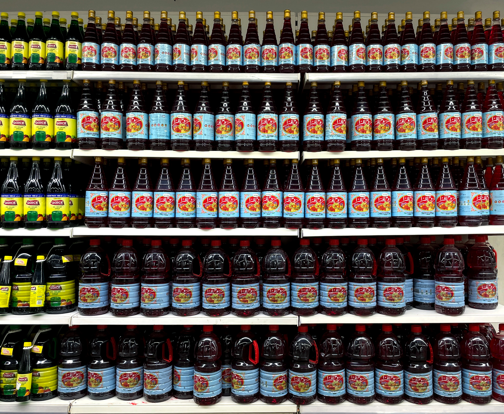 A photo of shelves in a superstore with rows and rows of rooh afza bottles in arranged in terms of size, biggest ones at the bottom