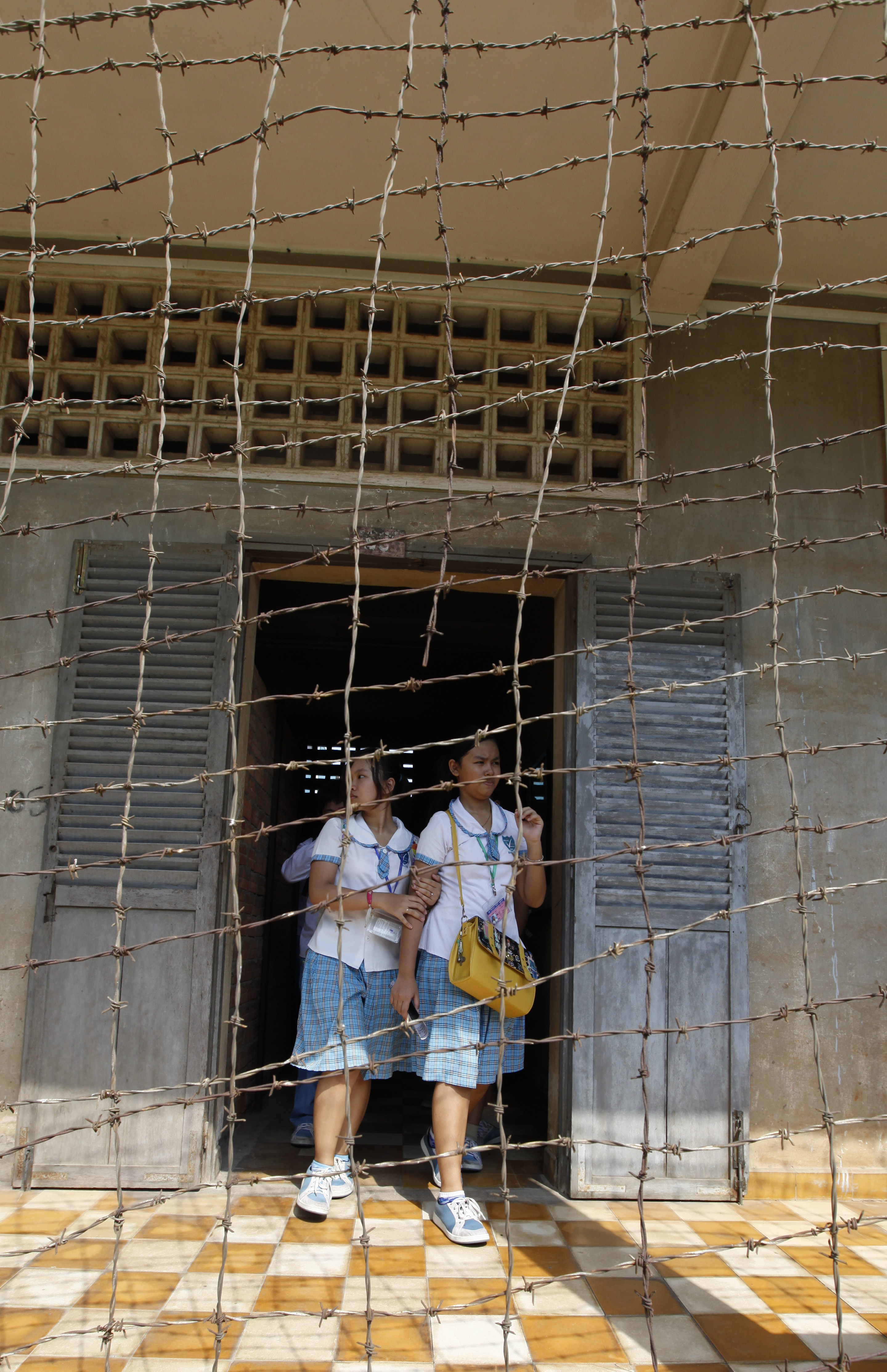 Two female students stand at a door behind rusted barbed wire as they visit the Tuol Sleng Genocide Centre from where the Khmer Rouge sent thousands of Cambodians to their deaths