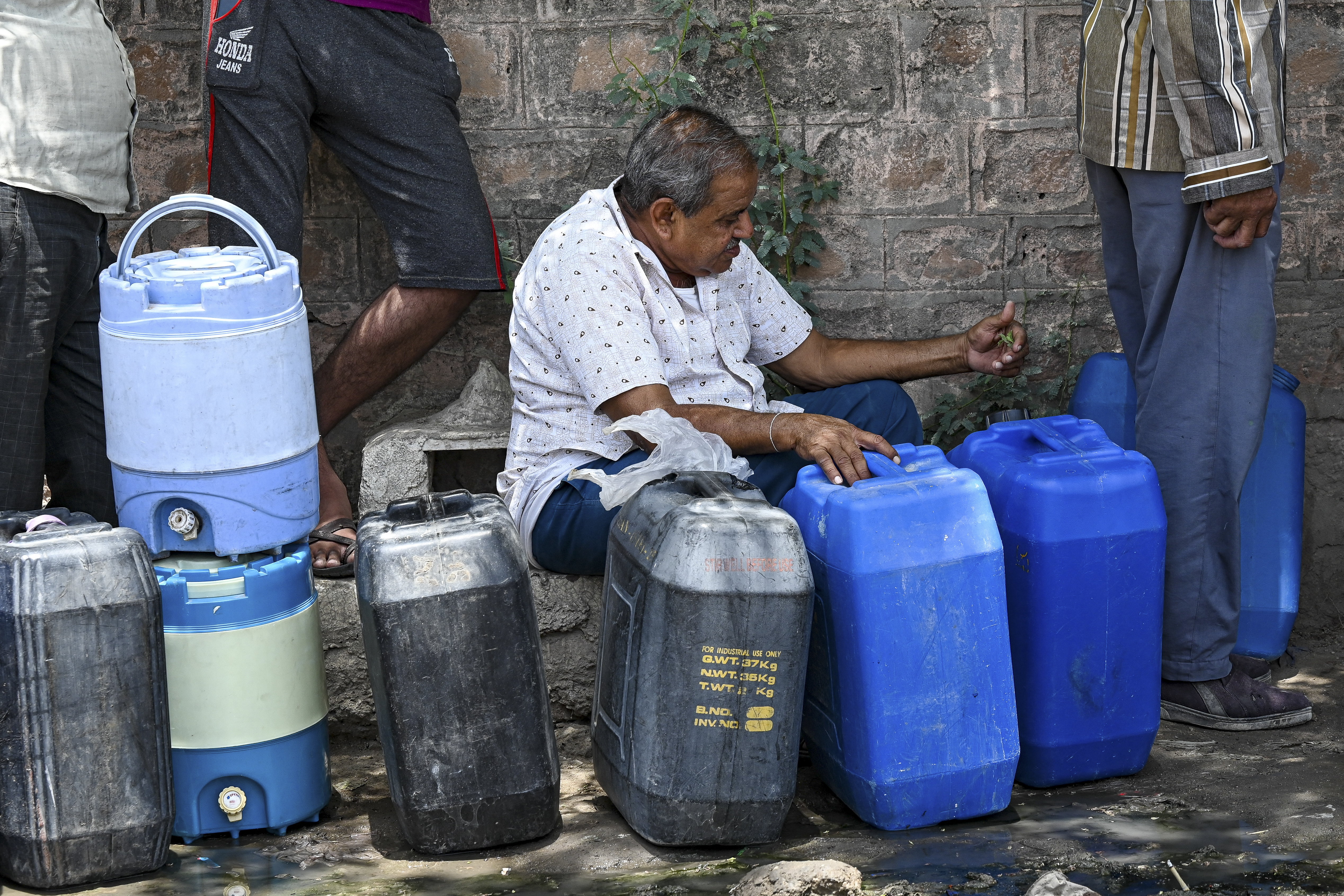 A man waiting to refill the containers with tap water supplied by the government on a hot summer day in Pali.