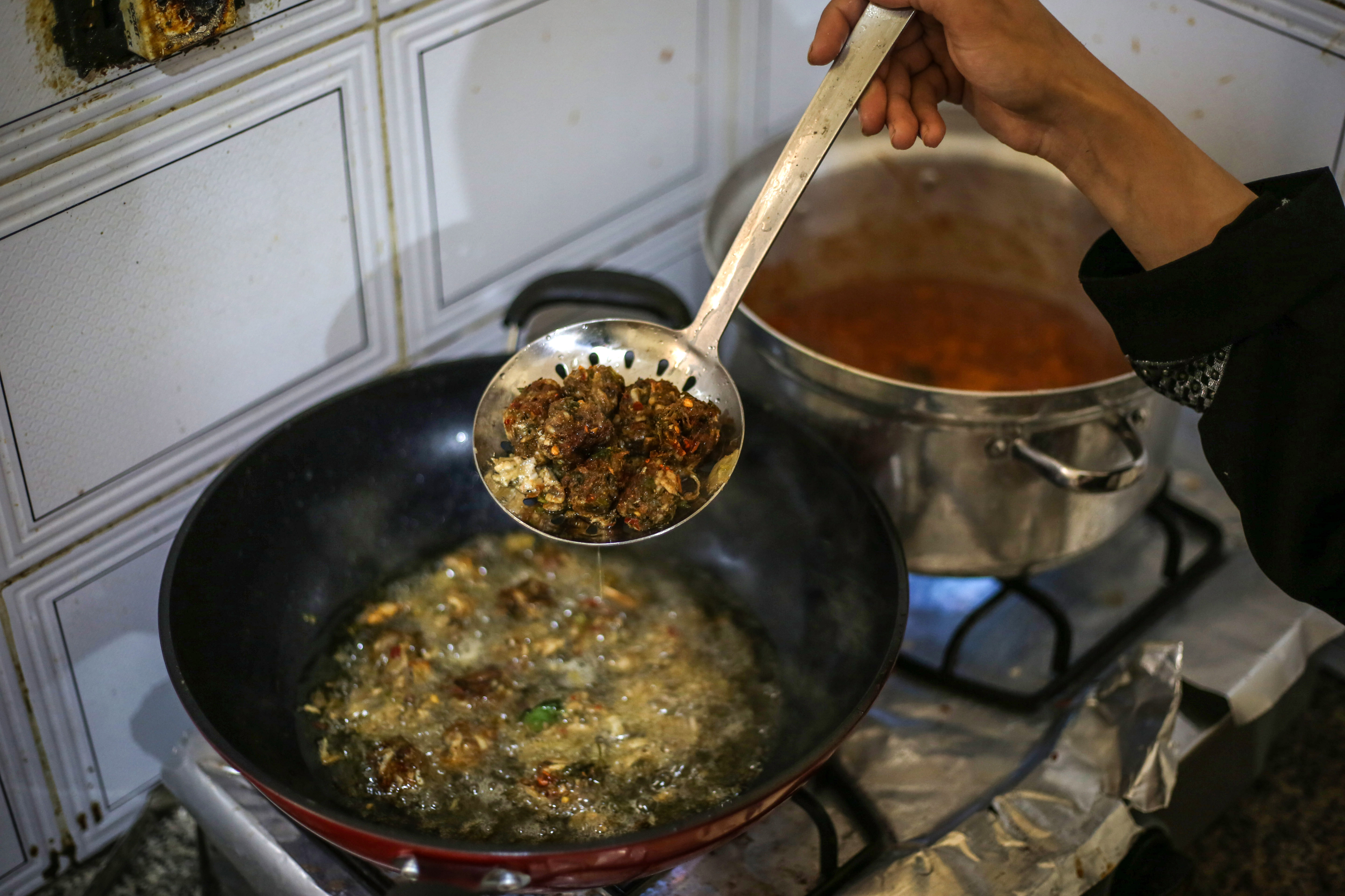 A hand holding a slotted spoon lifts some fish balls out of a wok full of bubbling oil
